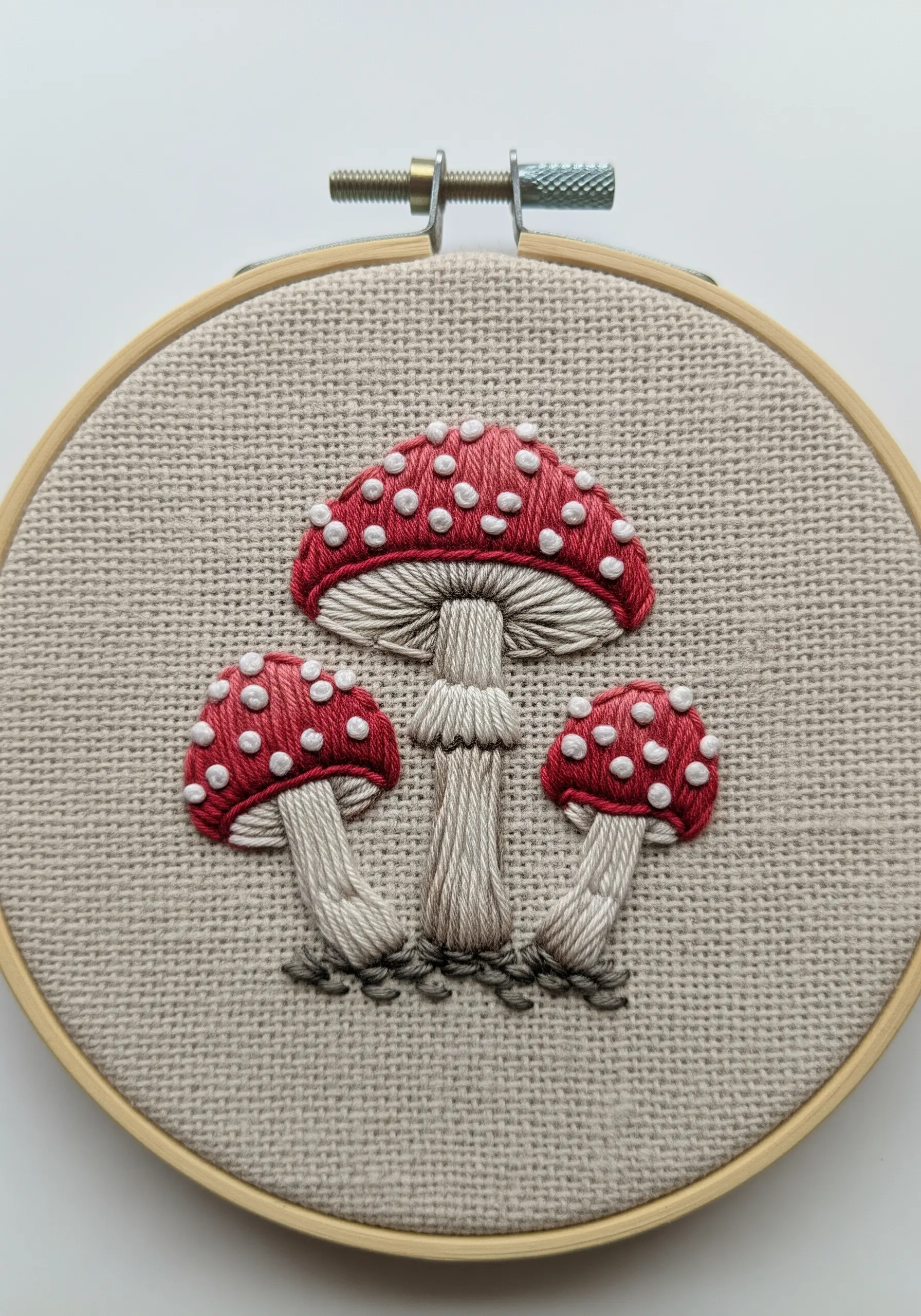 Three red-and-white amanita mushrooms embroidered with blended colors and French knots.