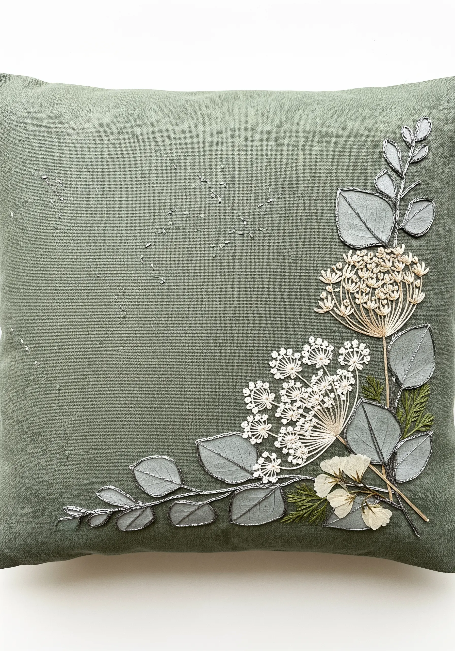 A sage green cushion corner adorned with pressed white flowers and embroidered silver leaves.