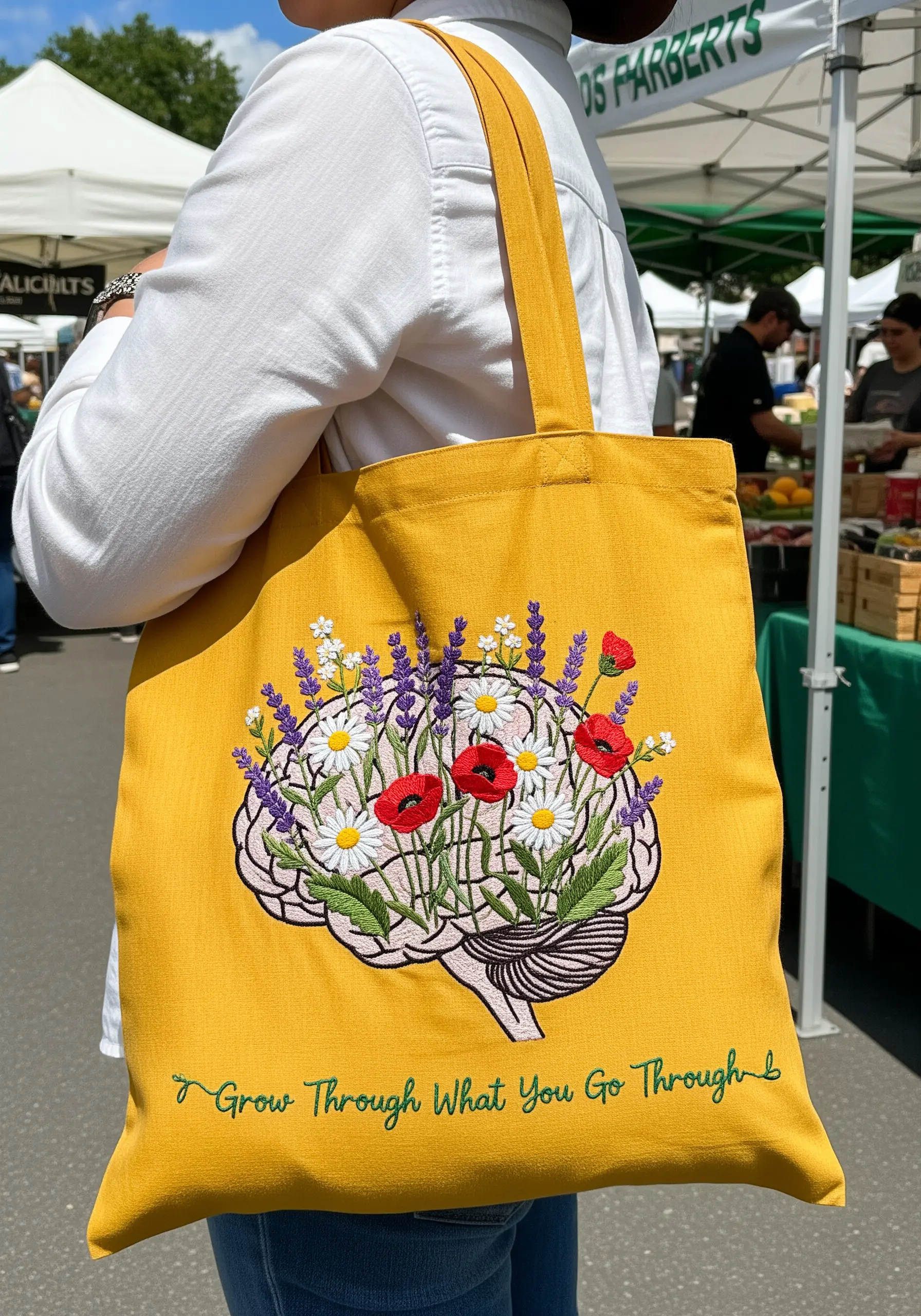 Embroidery of a brain filled with poppies, daisies, and lavender on a yellow tote bag.