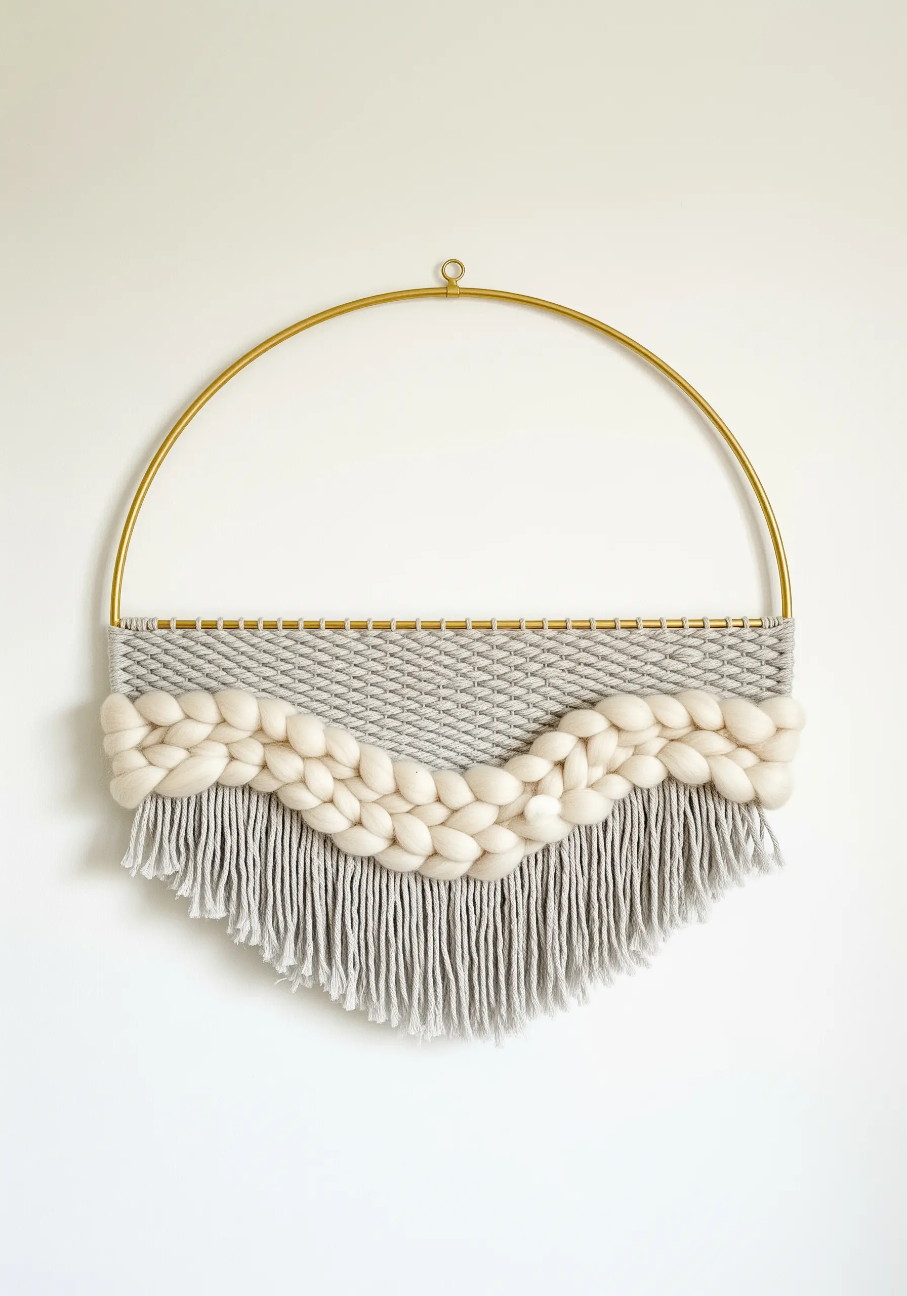 A circular woven wall hanging with grey yarn and a thick, creamy white wool roving braid.