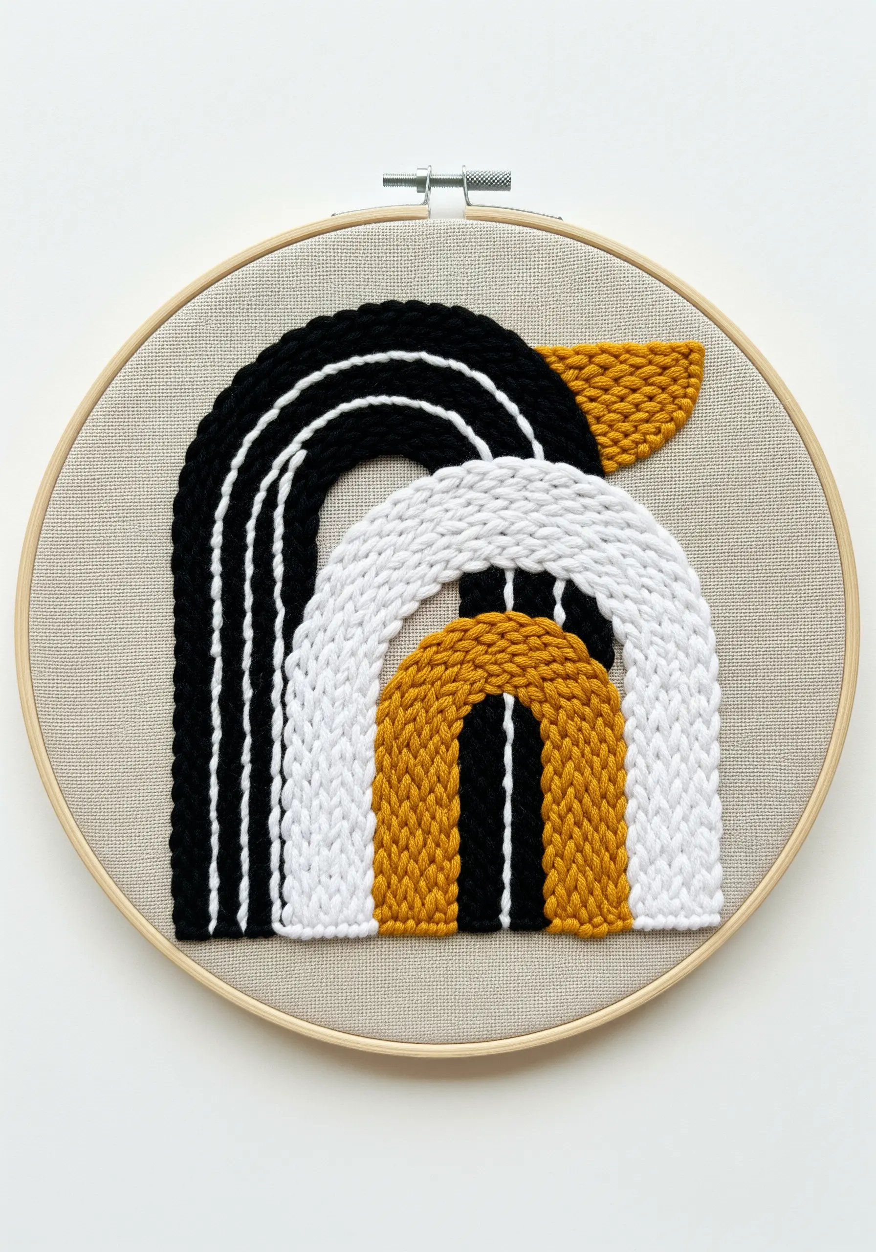 Abstract shapes in black, white, and gold yarn stitched in a wooden embroidery hoop.