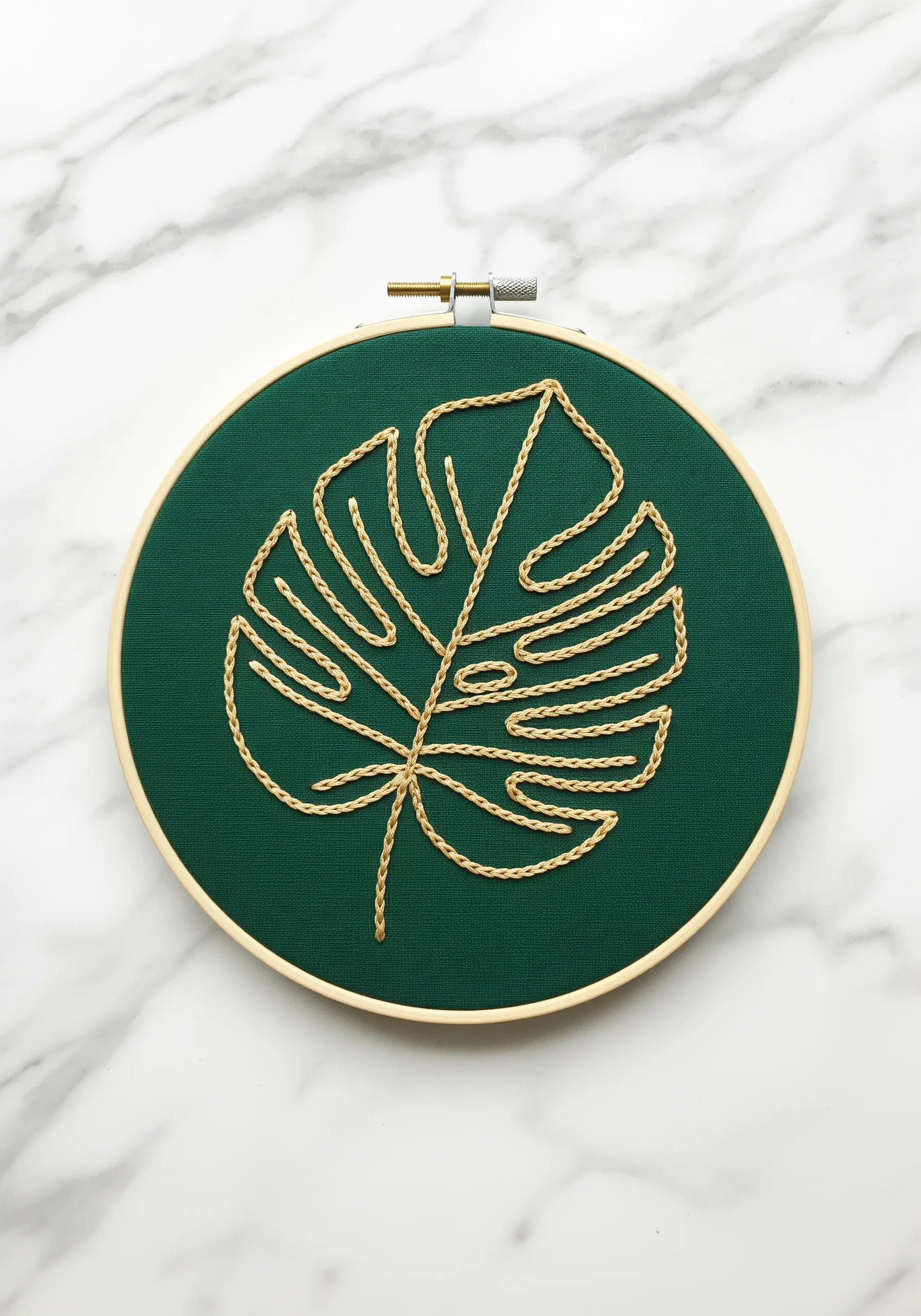 A monstera leaf outlined in a gold chain stitch on dark green fabric.