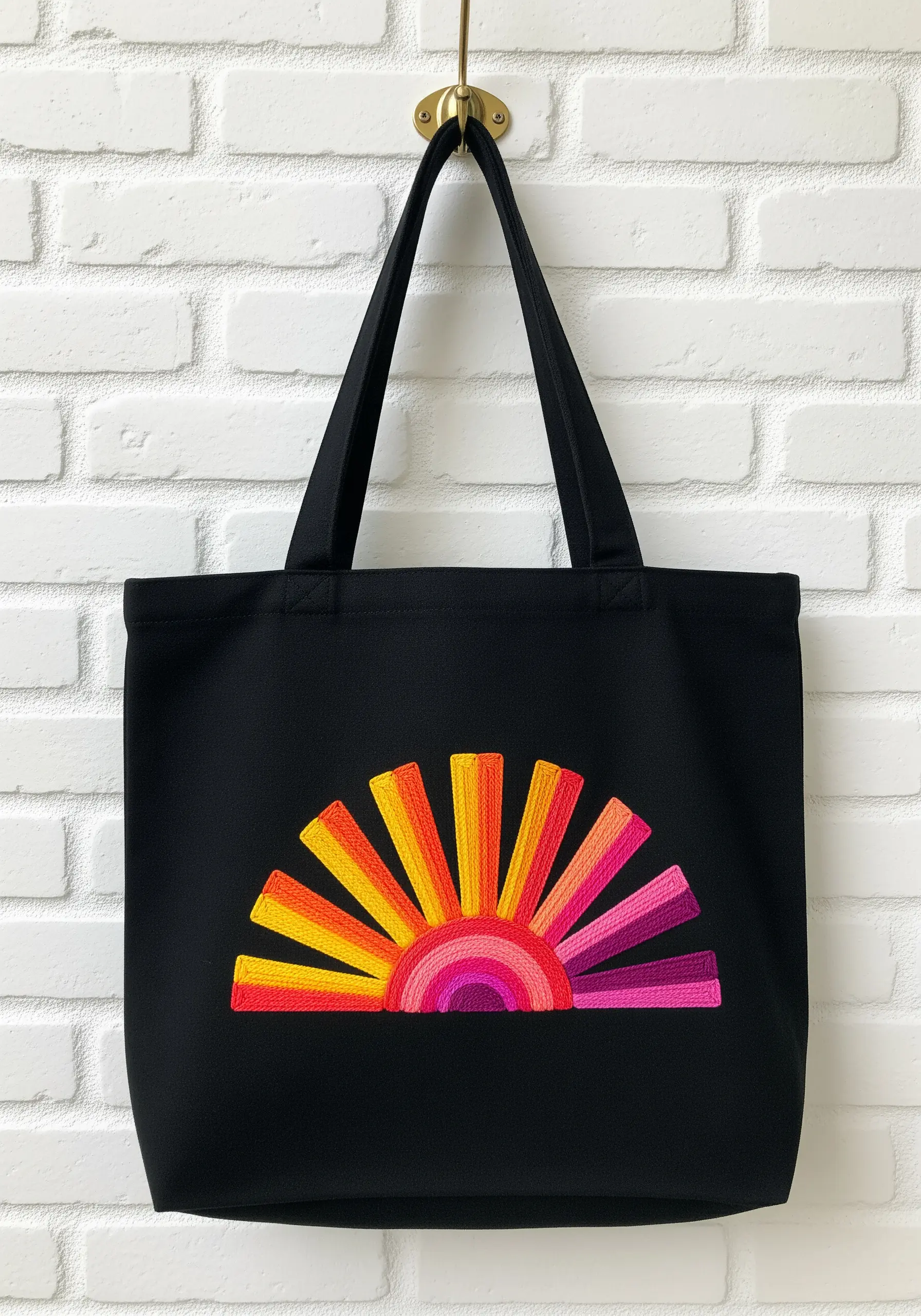 A vibrant sunrise motif with rays in shades of yellow, orange, and pink embroidered on a black tote bag.