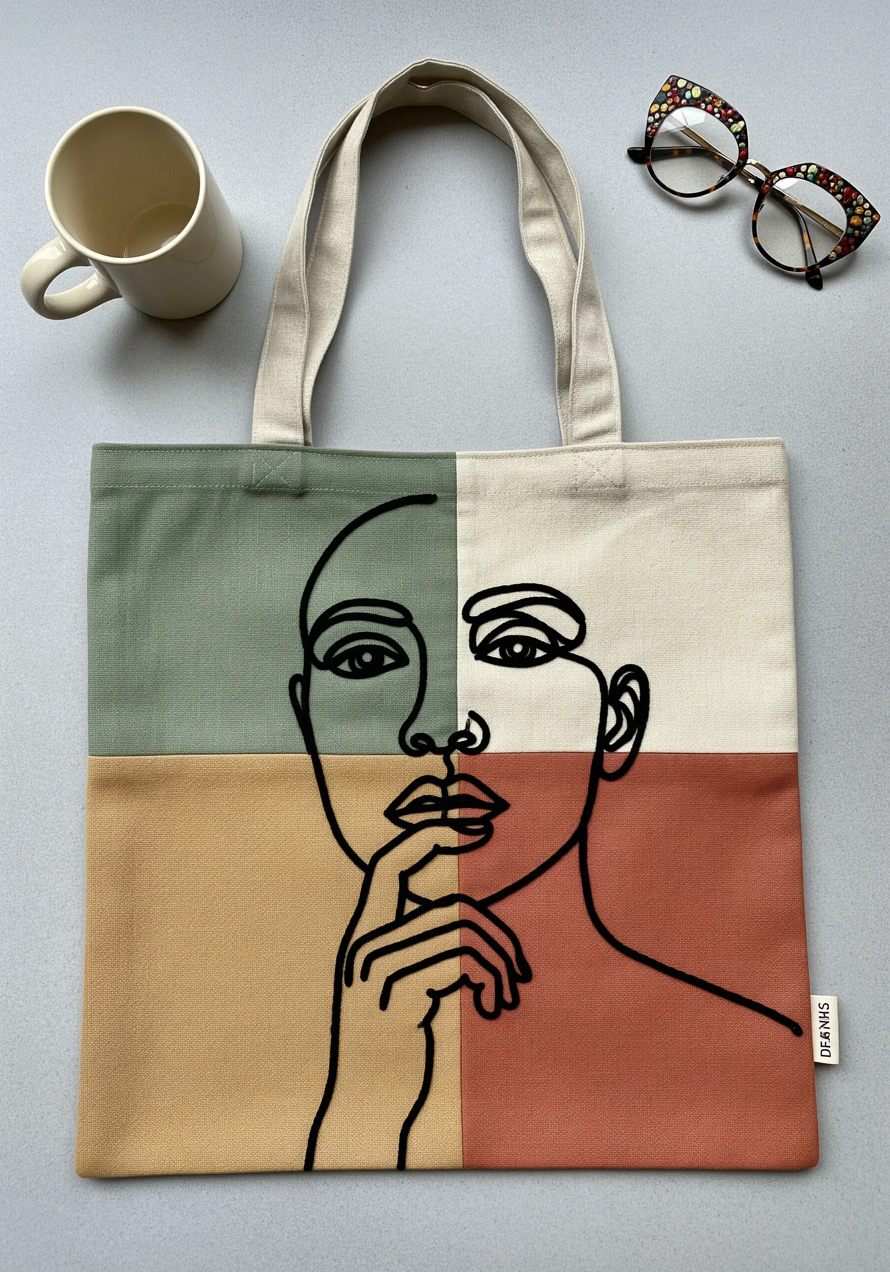 Minimalist single-line art portrait embroidered in black thread on a color-blocked tote bag.