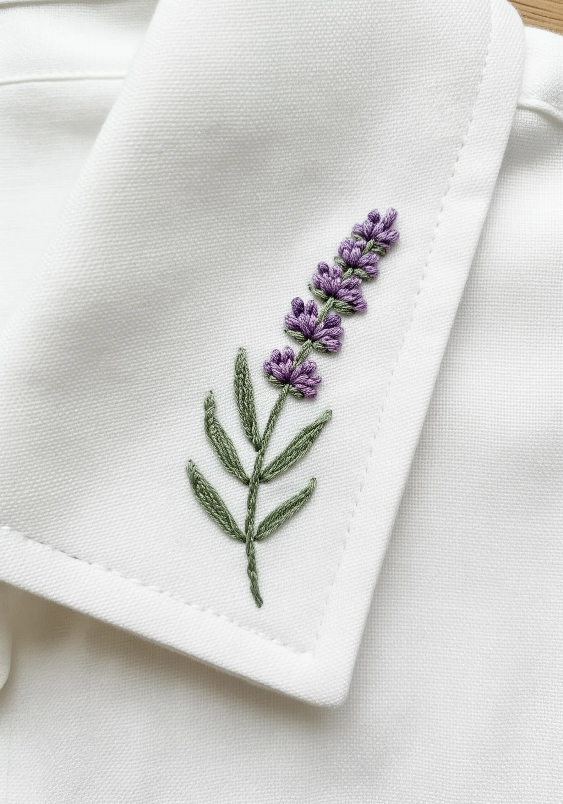 A delicate lavender sprig embroidered on the point of a white shirt collar.