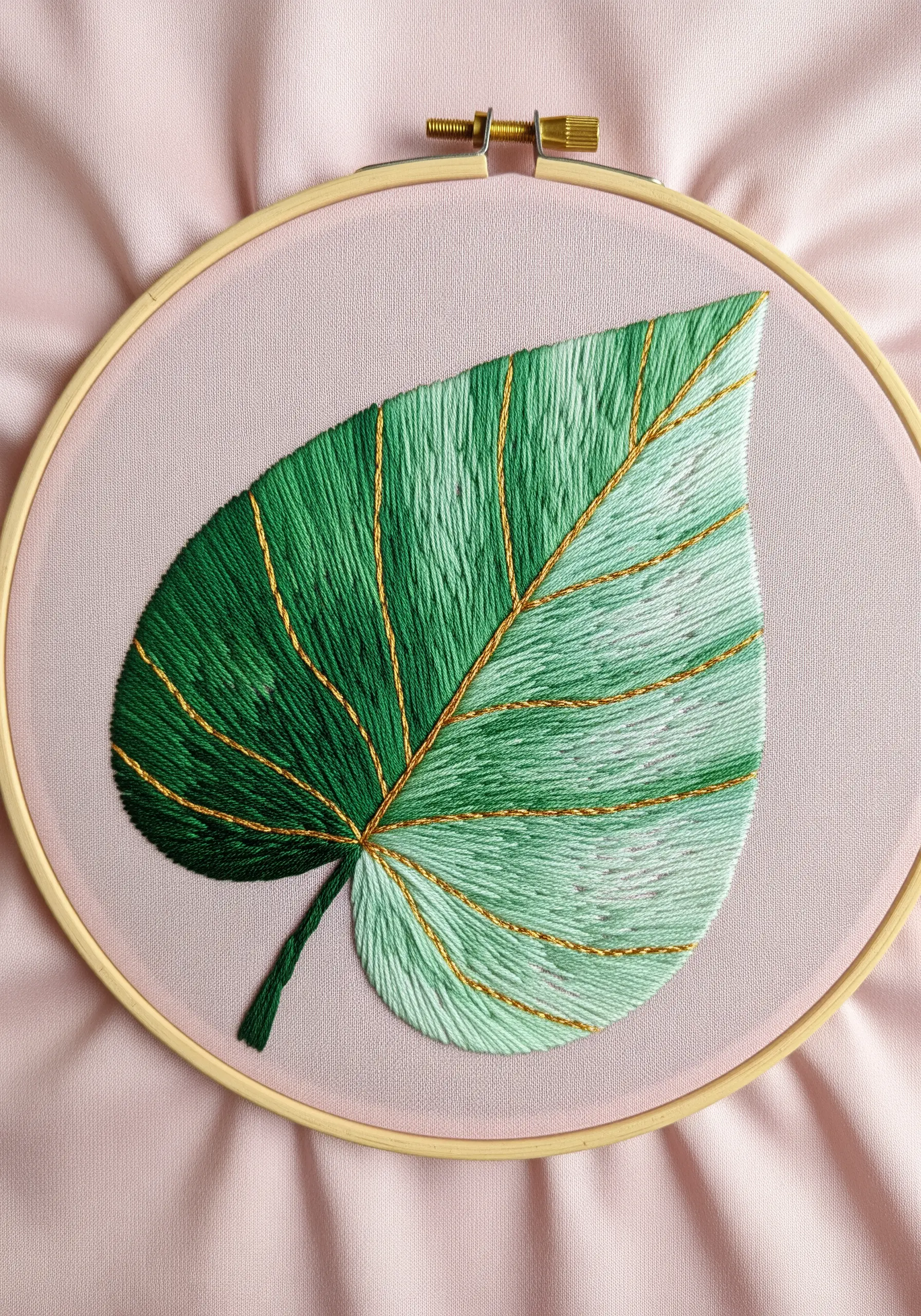 An embroidered leaf with a smooth green gradient and delicate gold metallic thread veins.