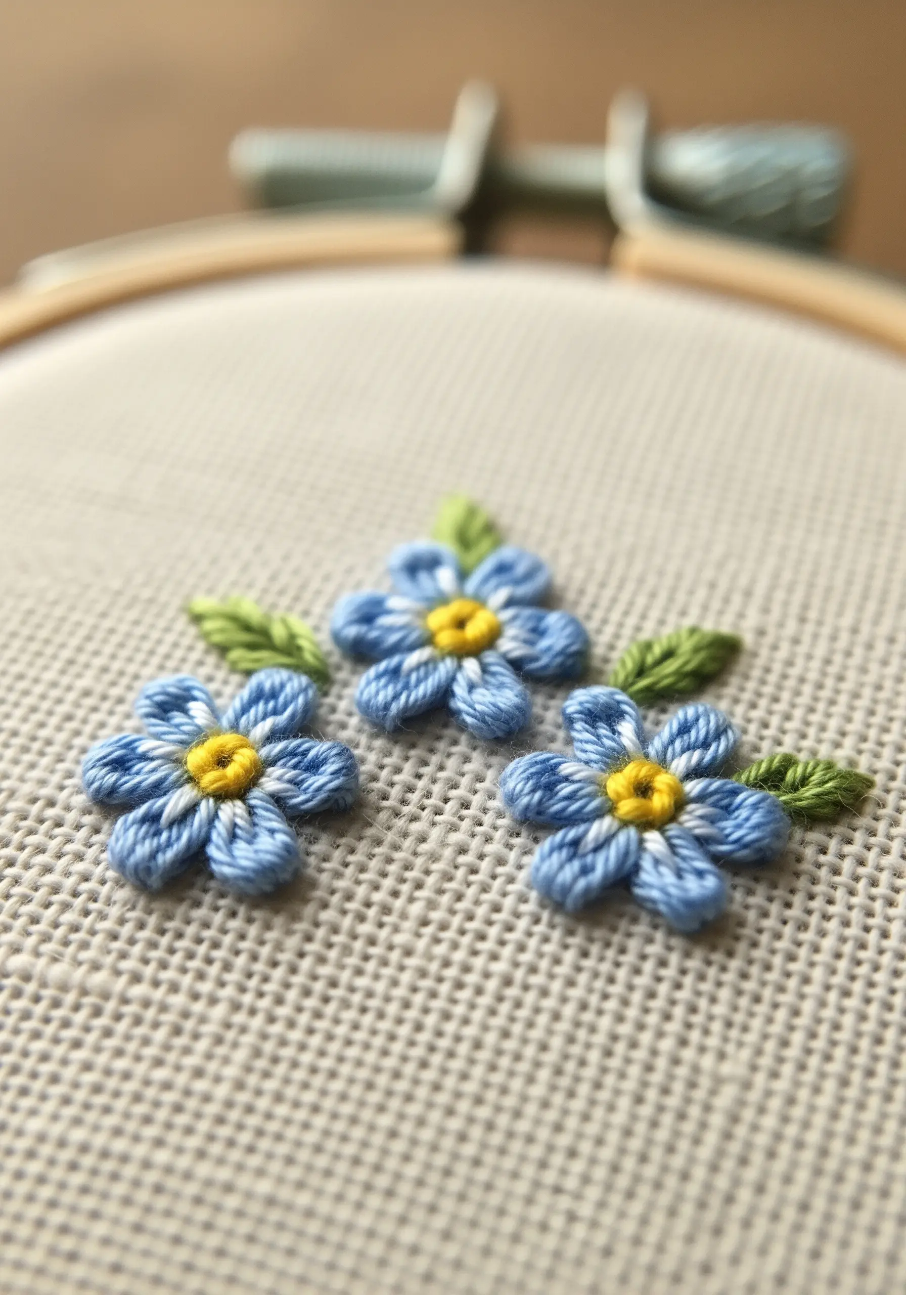 Three-dimensional blue forget-me-not flowers with yellow centers stitched on Aida cloth.