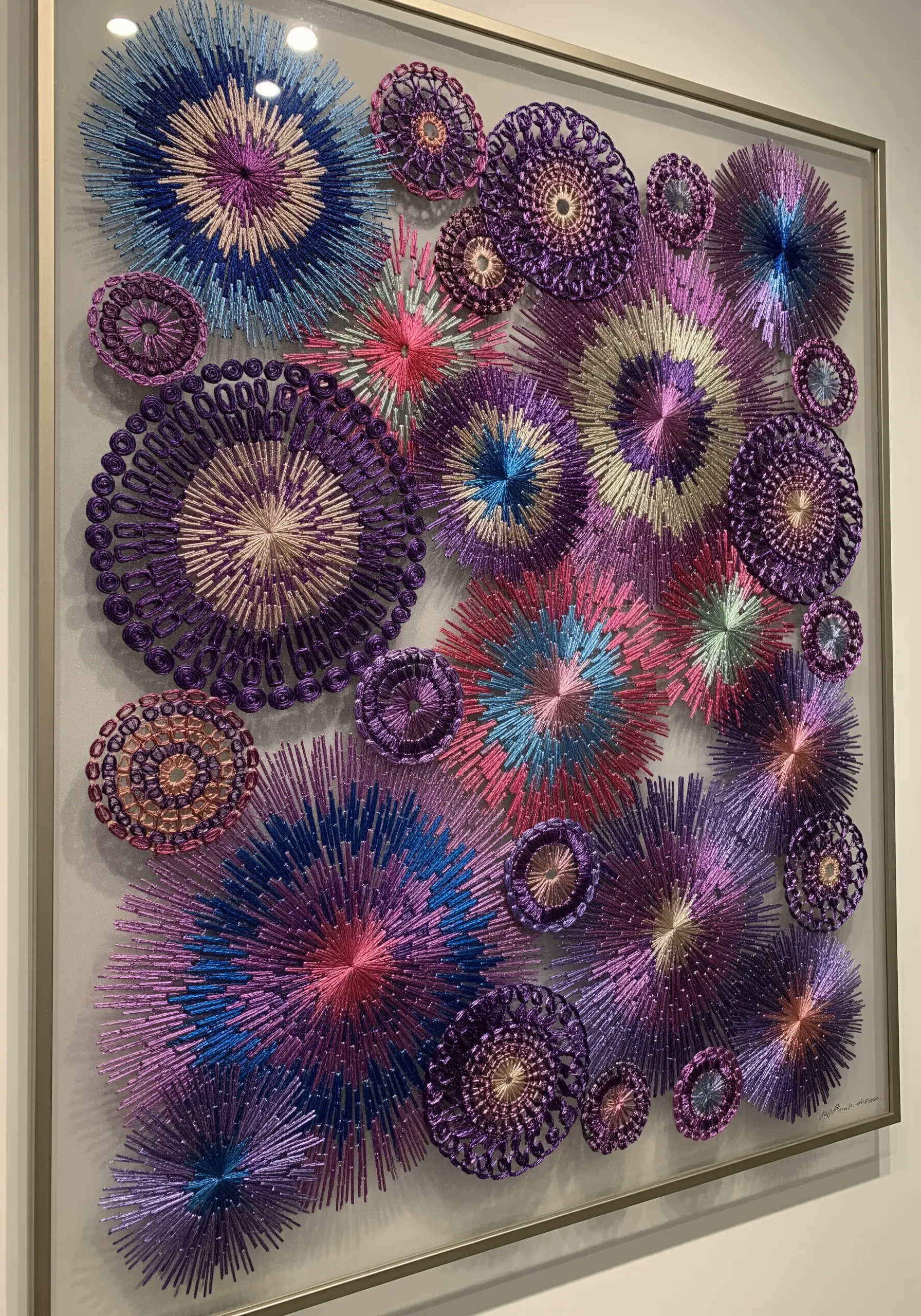 A framed collection of embroidered circular medallions in metallic purple, blue, and gold threads.