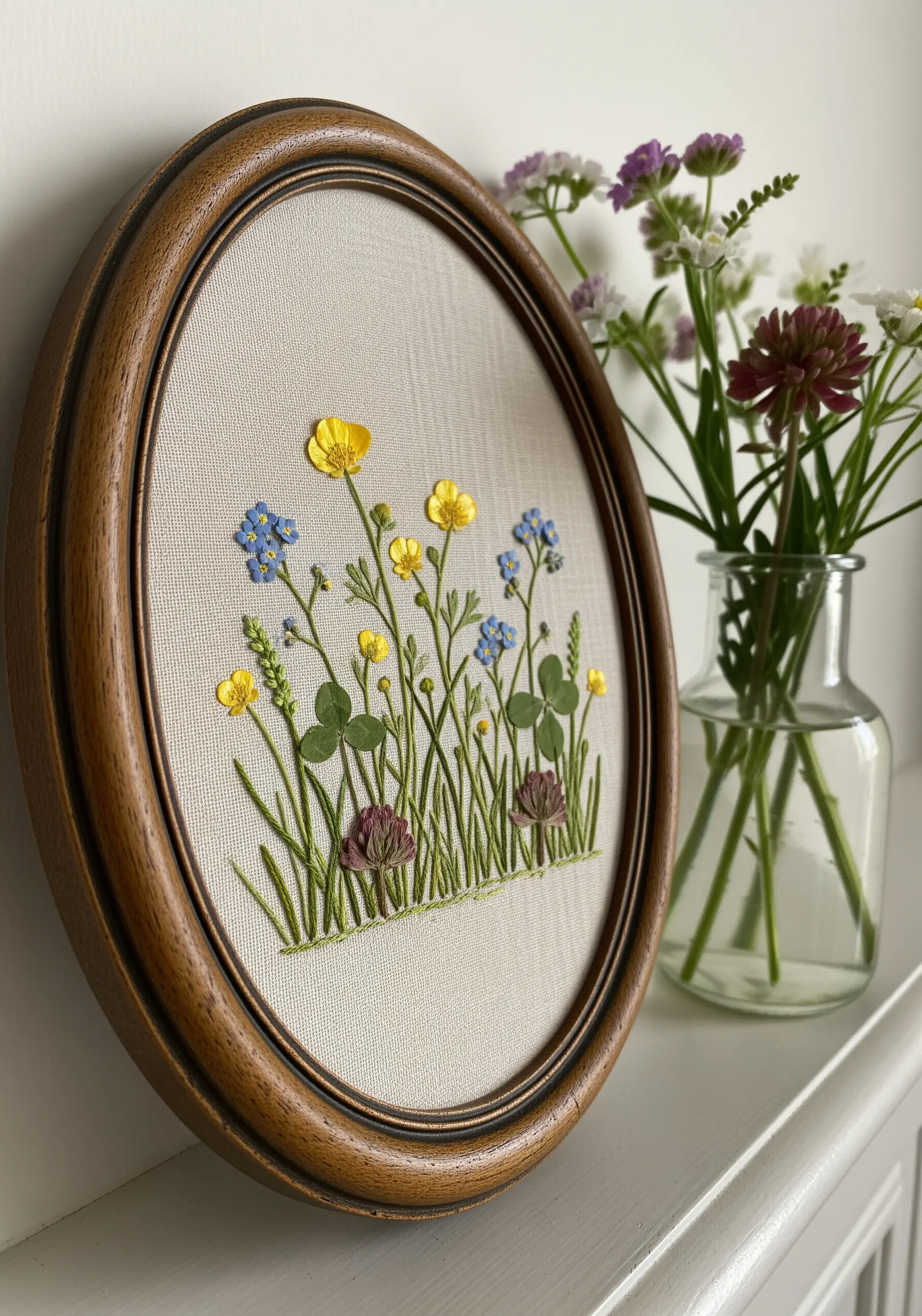 A wildflower scene in an oval frame, mixing pressed flowers with embroidered versions.