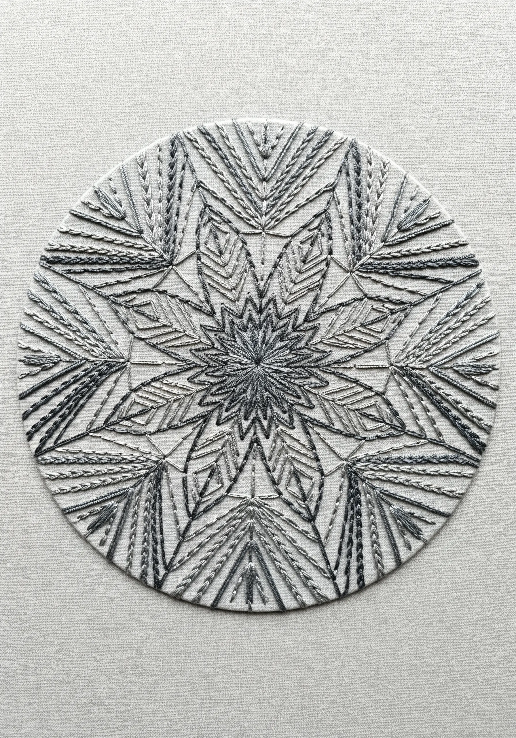 A detailed monochrome mandala embroidered with various textural stitches in shades of grey.