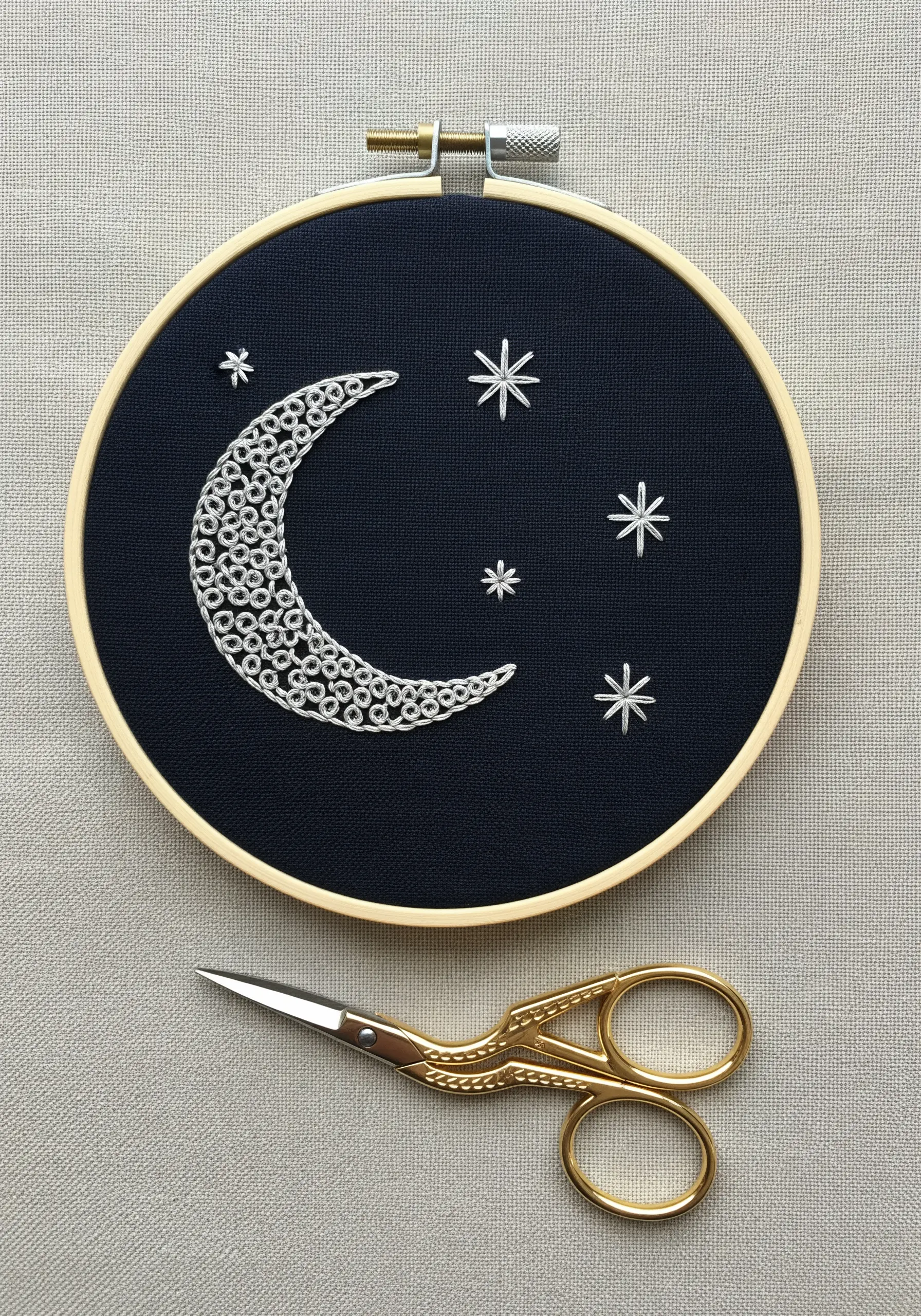 A crescent moon filled with dense silver French knots on dark navy fabric.