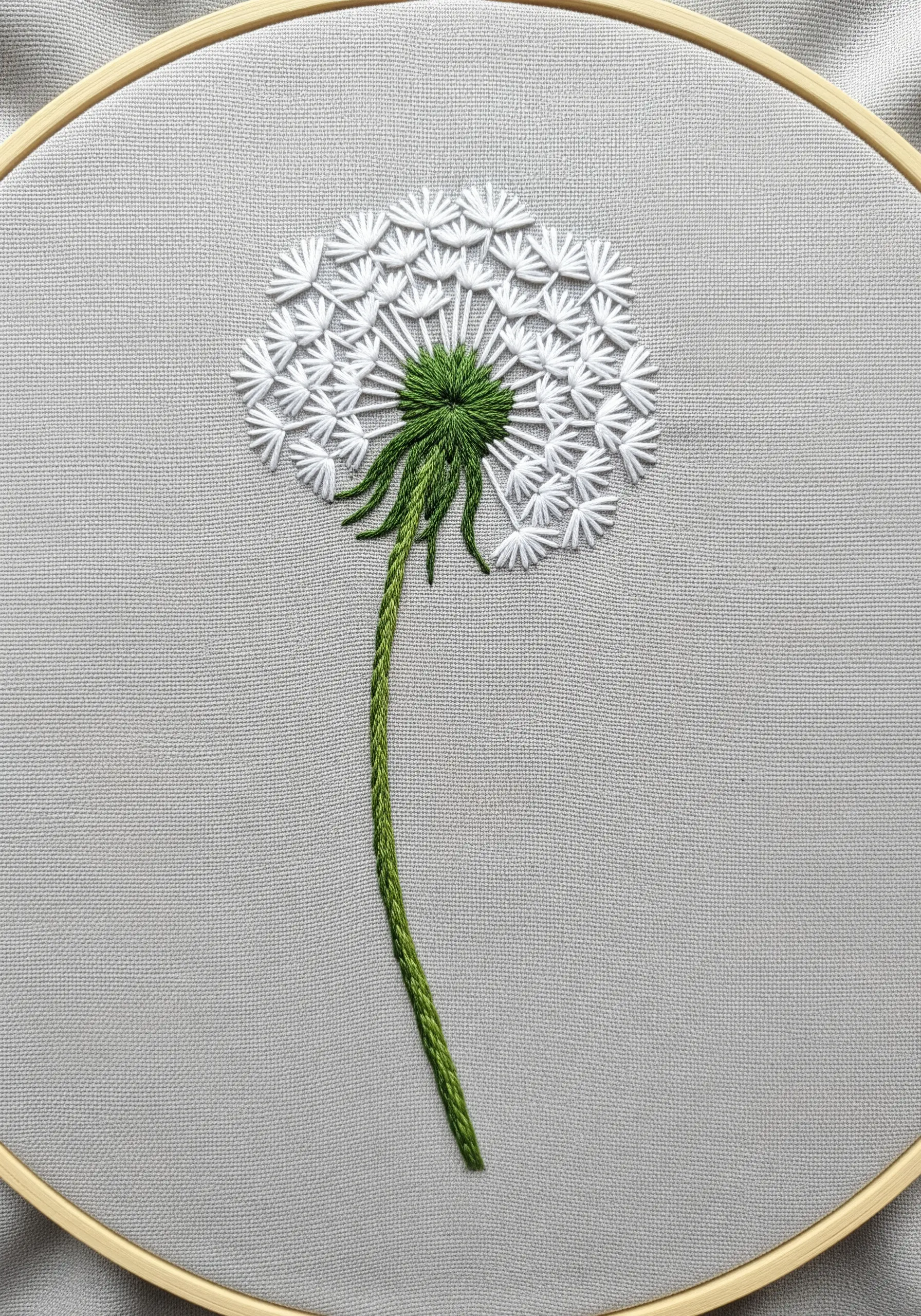 An embroidered dandelion seed head on gray fabric, made with white lazy daisy stitches.