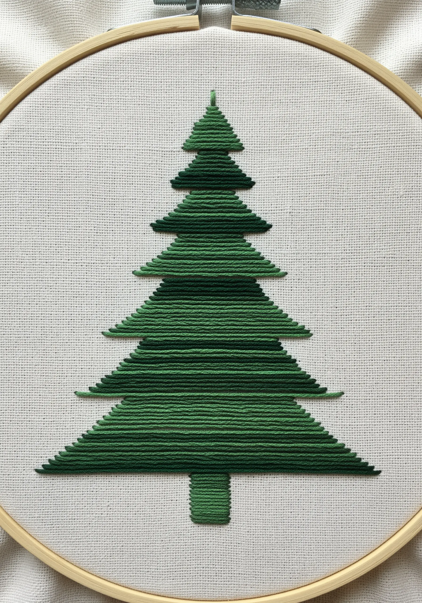 A geometric Christmas tree made of horizontal straight stitches in a single shade of green.