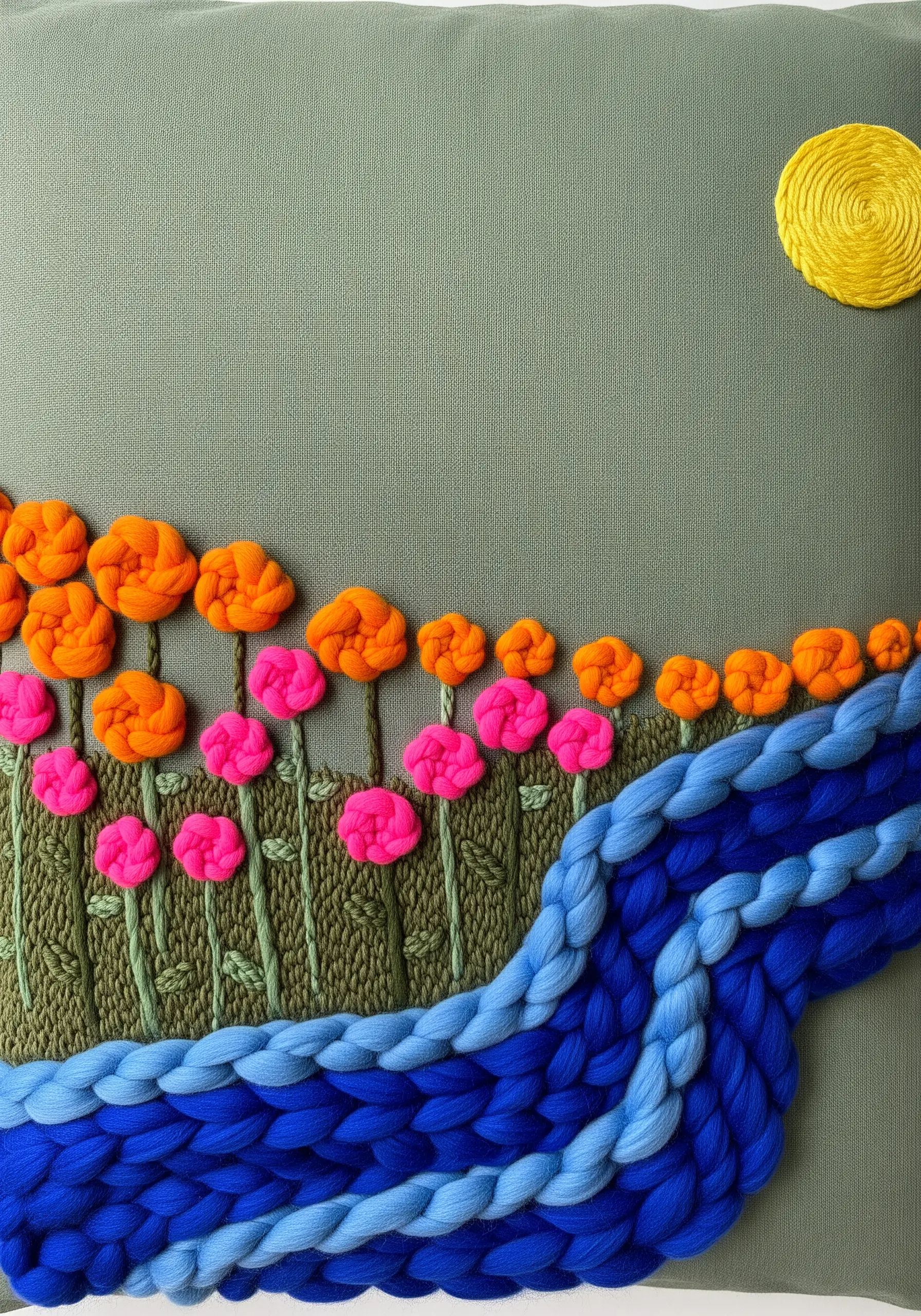 Textured landscape with woven blue yarn river and 3D woven wheel flowers.