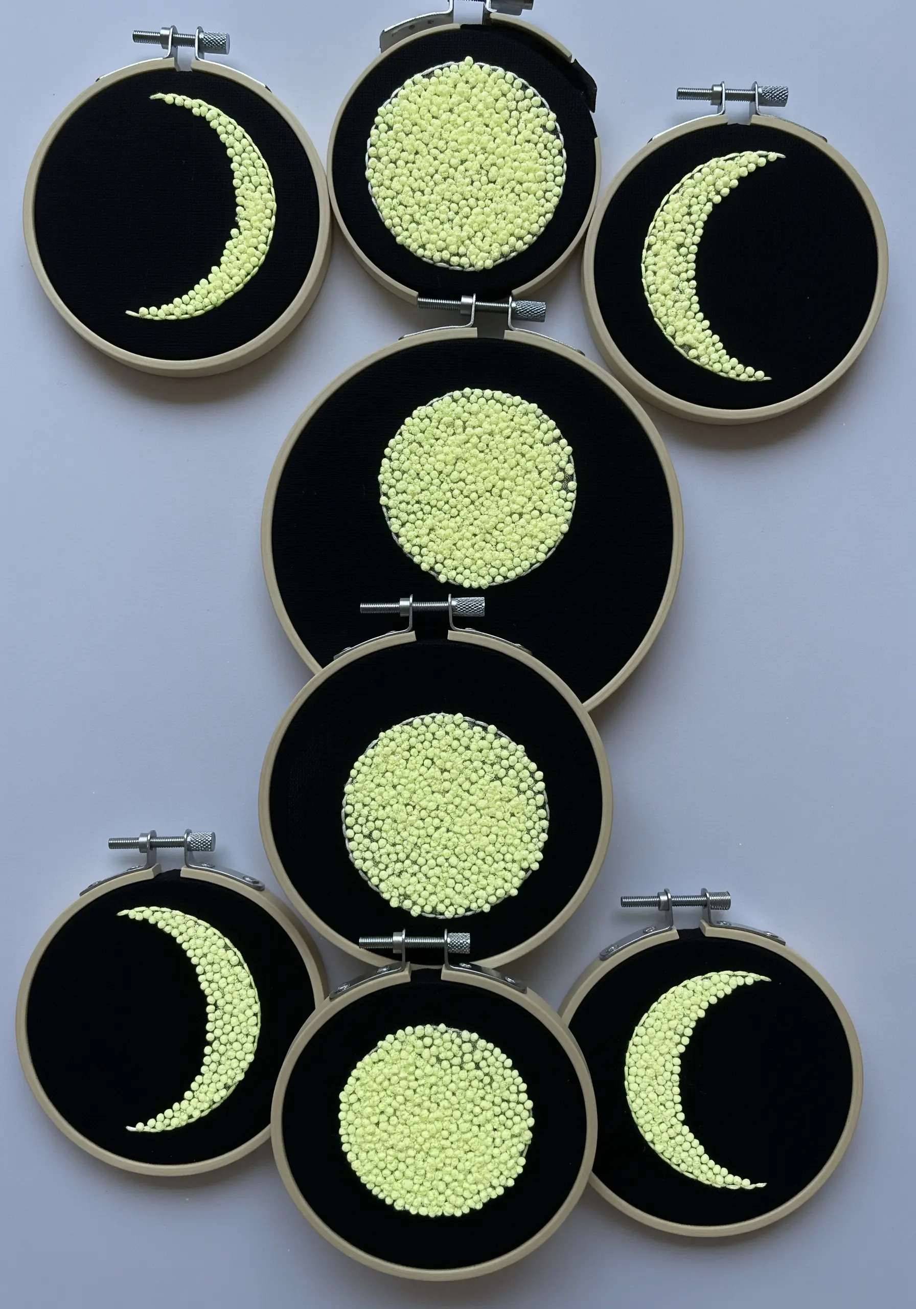 Moon phases created with dense, glow-in-the-dark yellow beads in embroidery hoops.