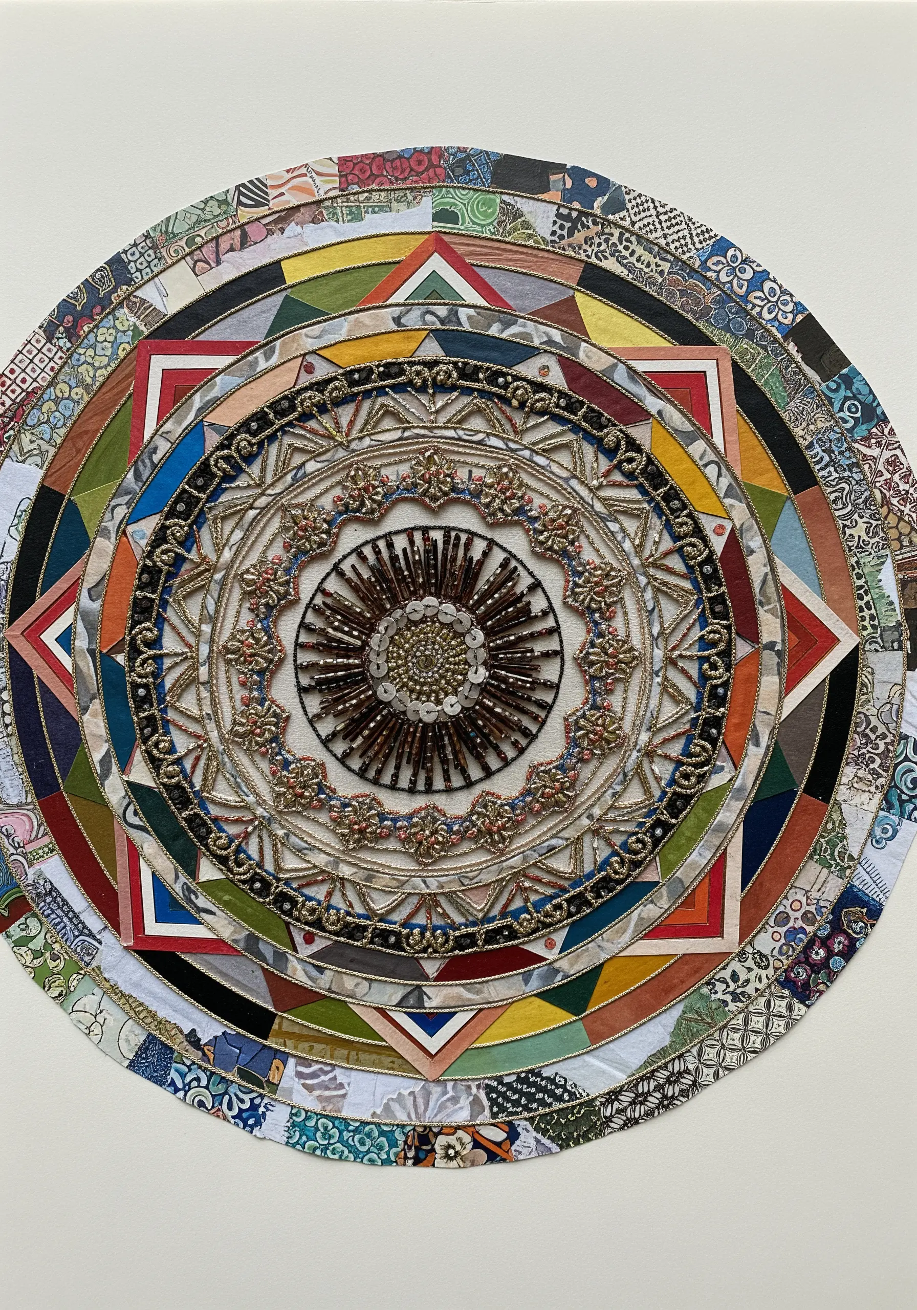 A large, circular mandala made from layered fabric scraps, beads, and couched metallic thread.