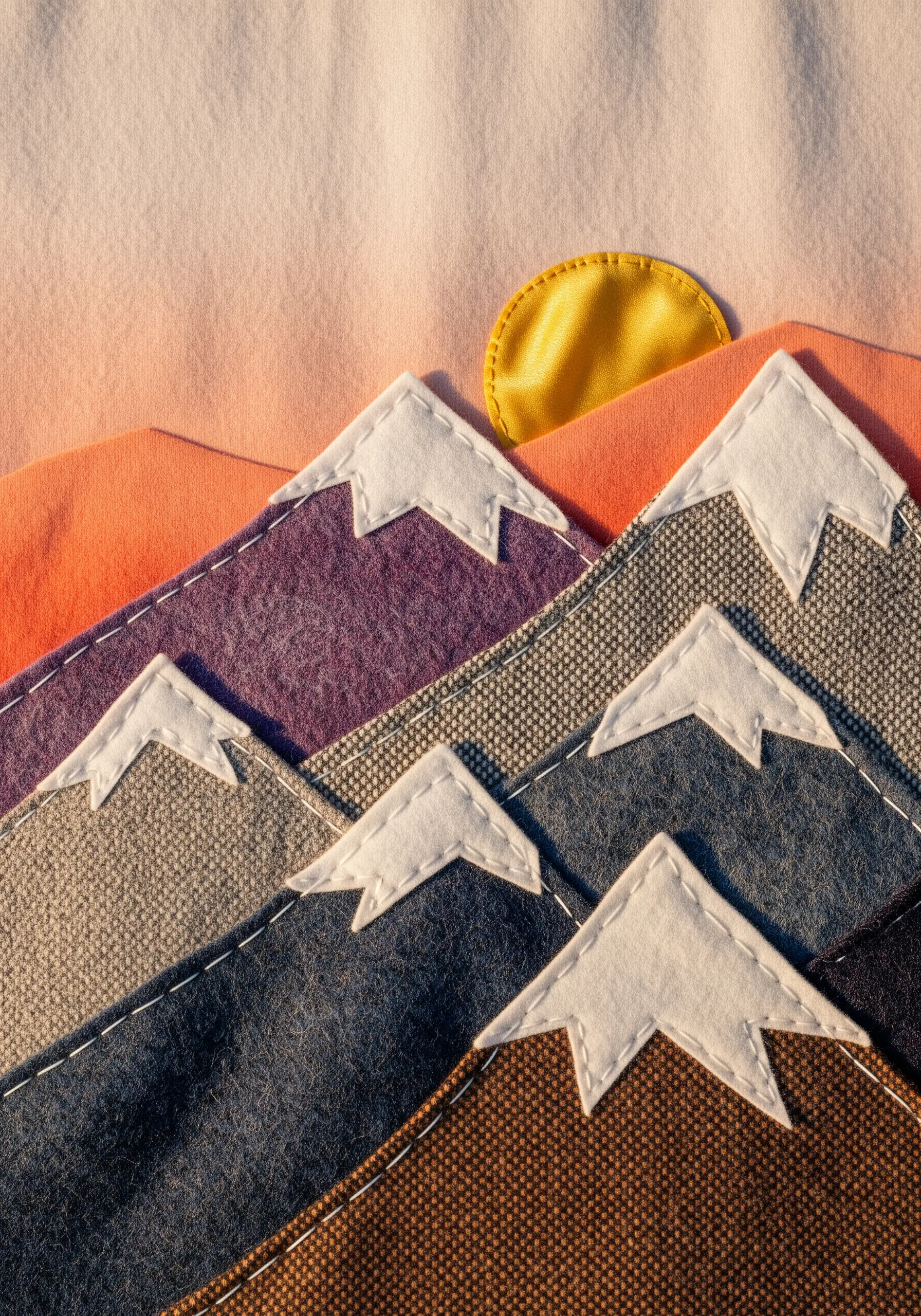 A layered fabric collage depicting a mountain range at sunrise, with stitched snow caps.