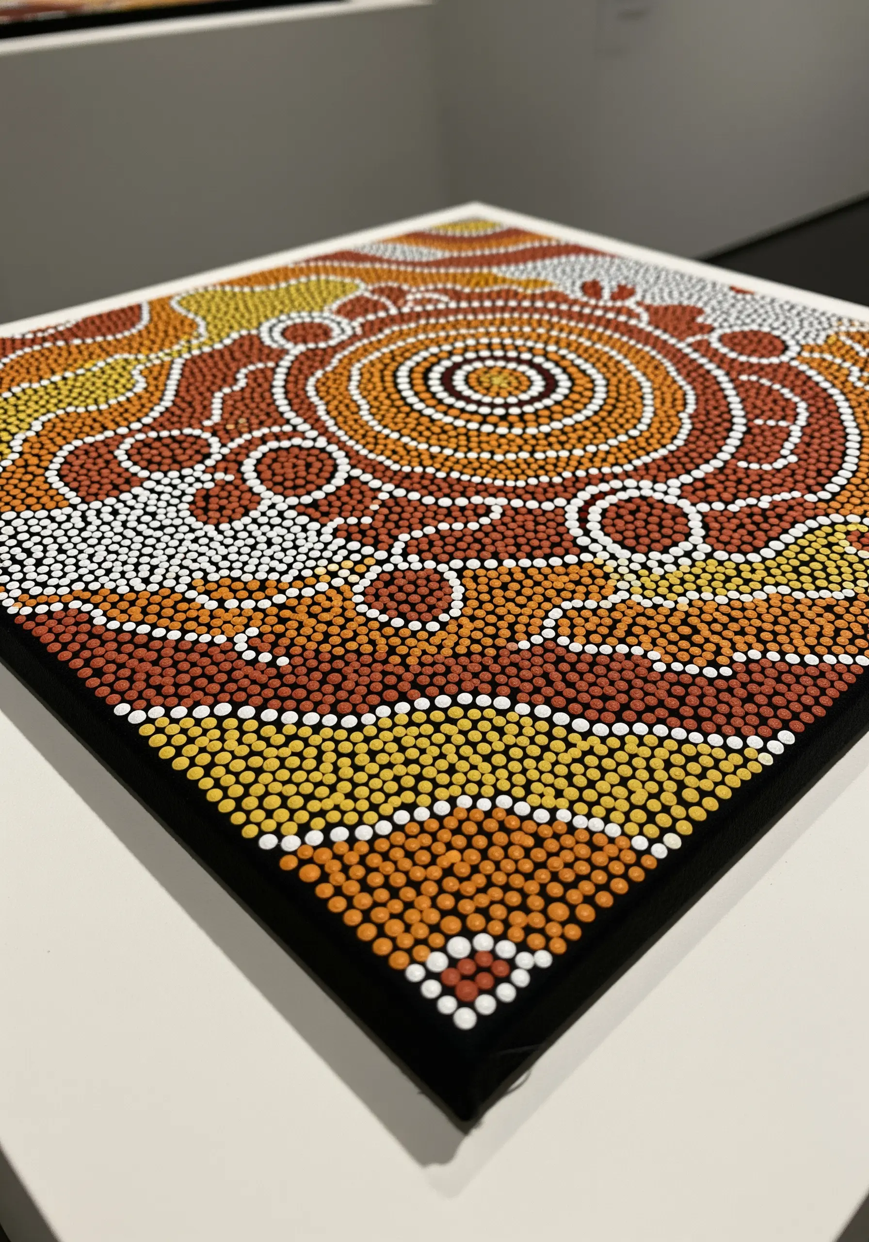 An Aboriginal-style dot painting on canvas with concentric circles in earthy tones.