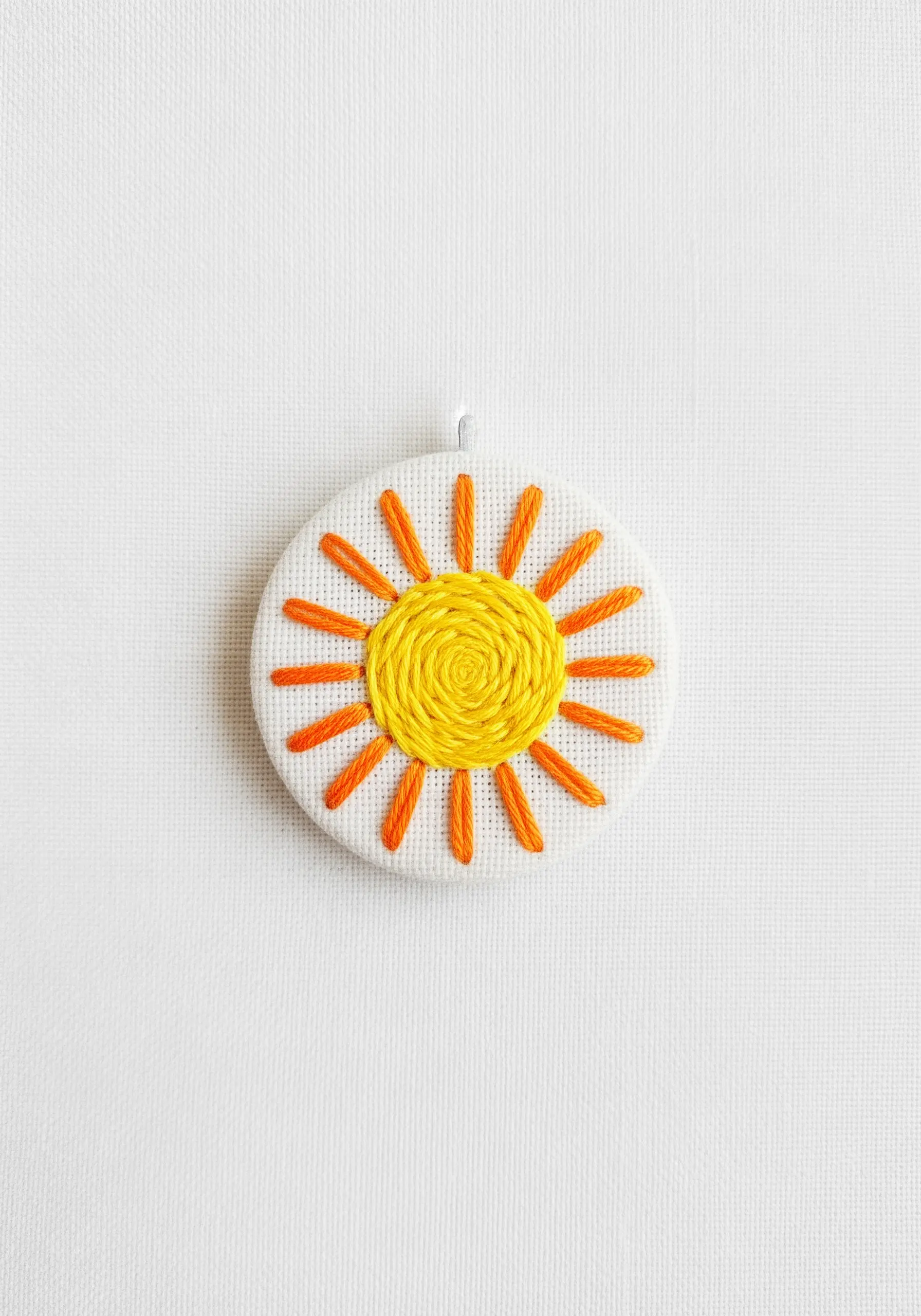An embroidered sun with a textured yellow spiral center and orange straight-stitch rays.