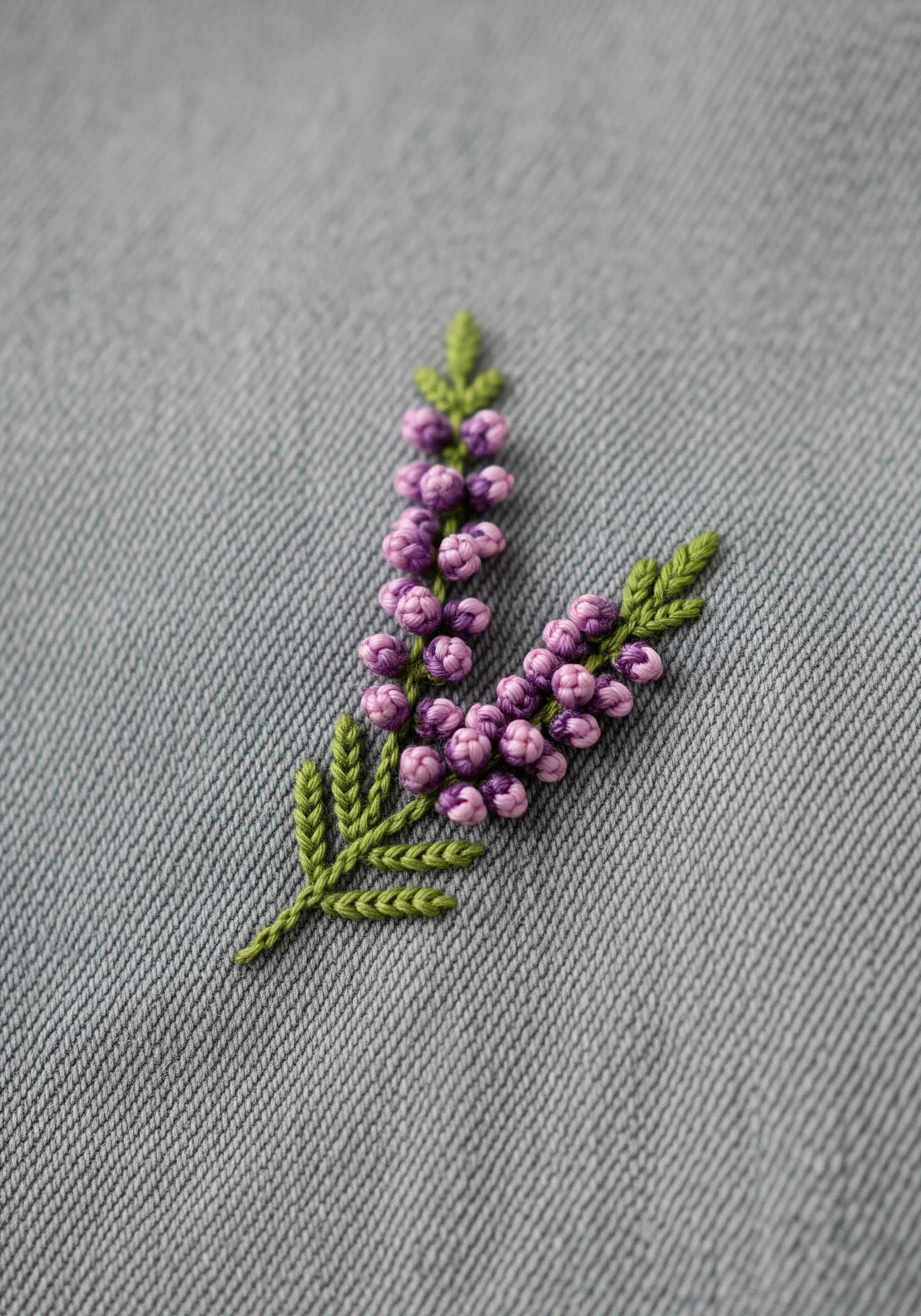 Two sprigs of heather with purple and pink colonial knots on light gray-blue denim.
