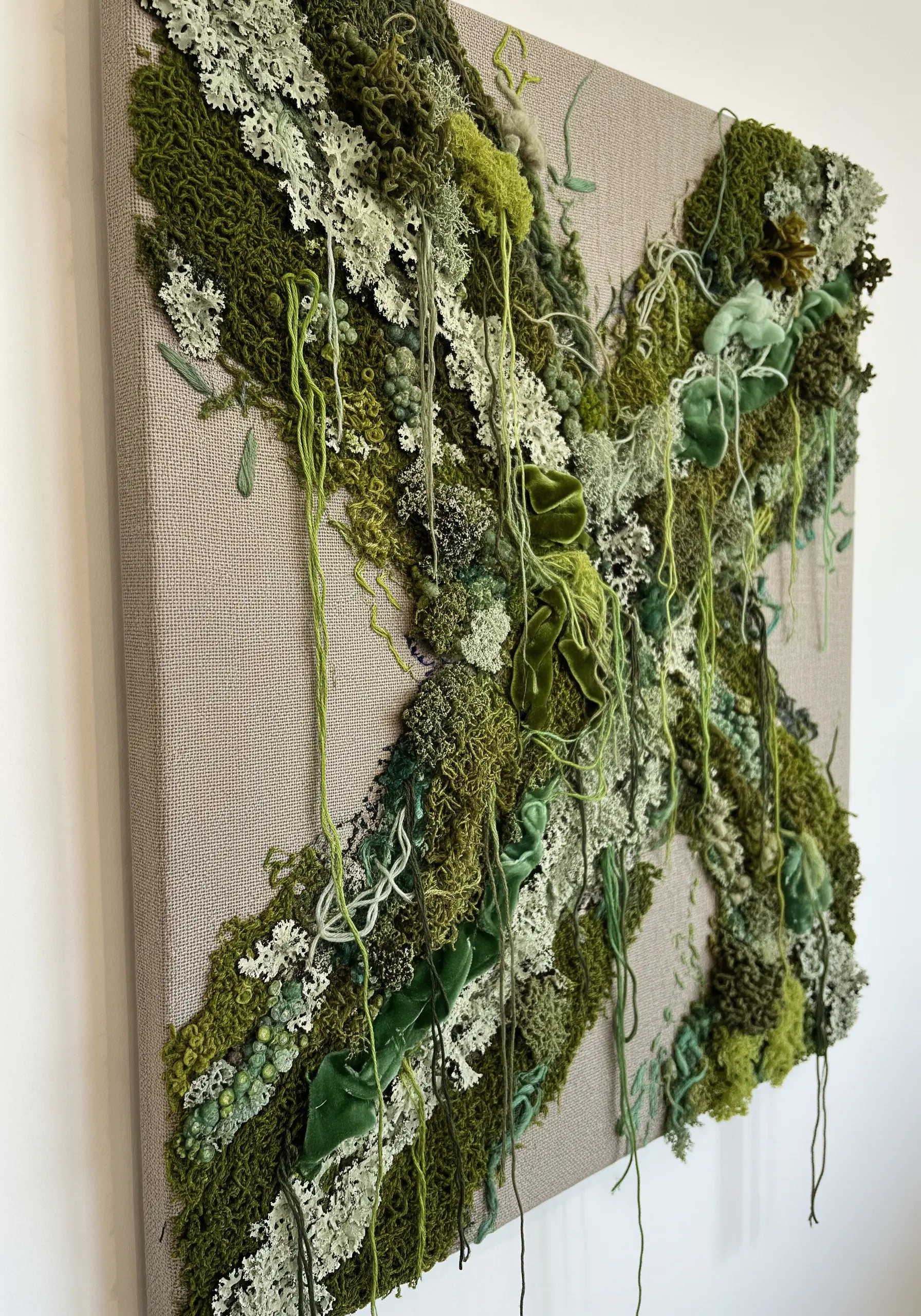 A 3D textile art piece with various green fibers creating a lush, moss-like texture.
