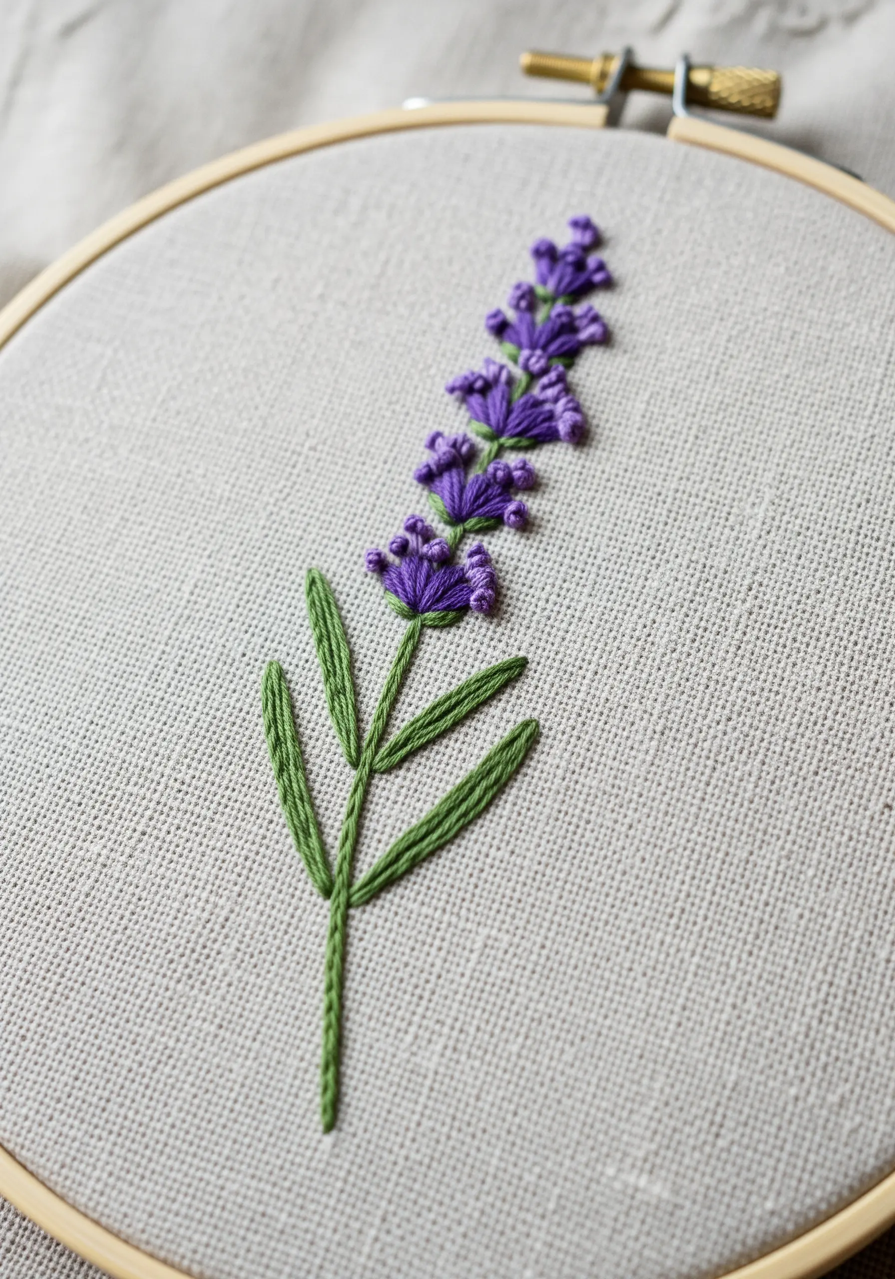 An embroidered sprig of lavender with purple French knots on natural linen fabric.