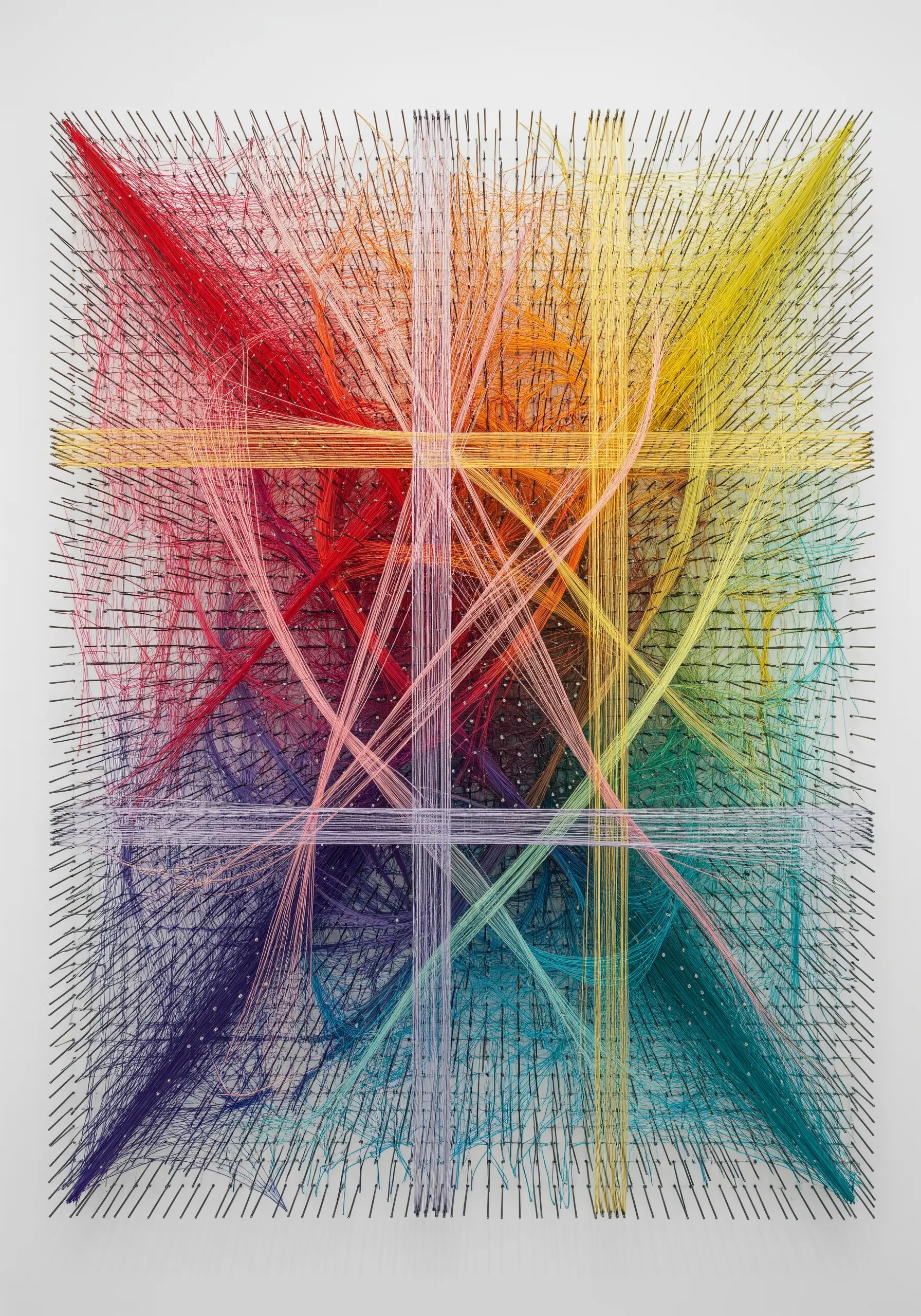 A complex string art piece with rainbow-colored threads stretched between a grid of nails.