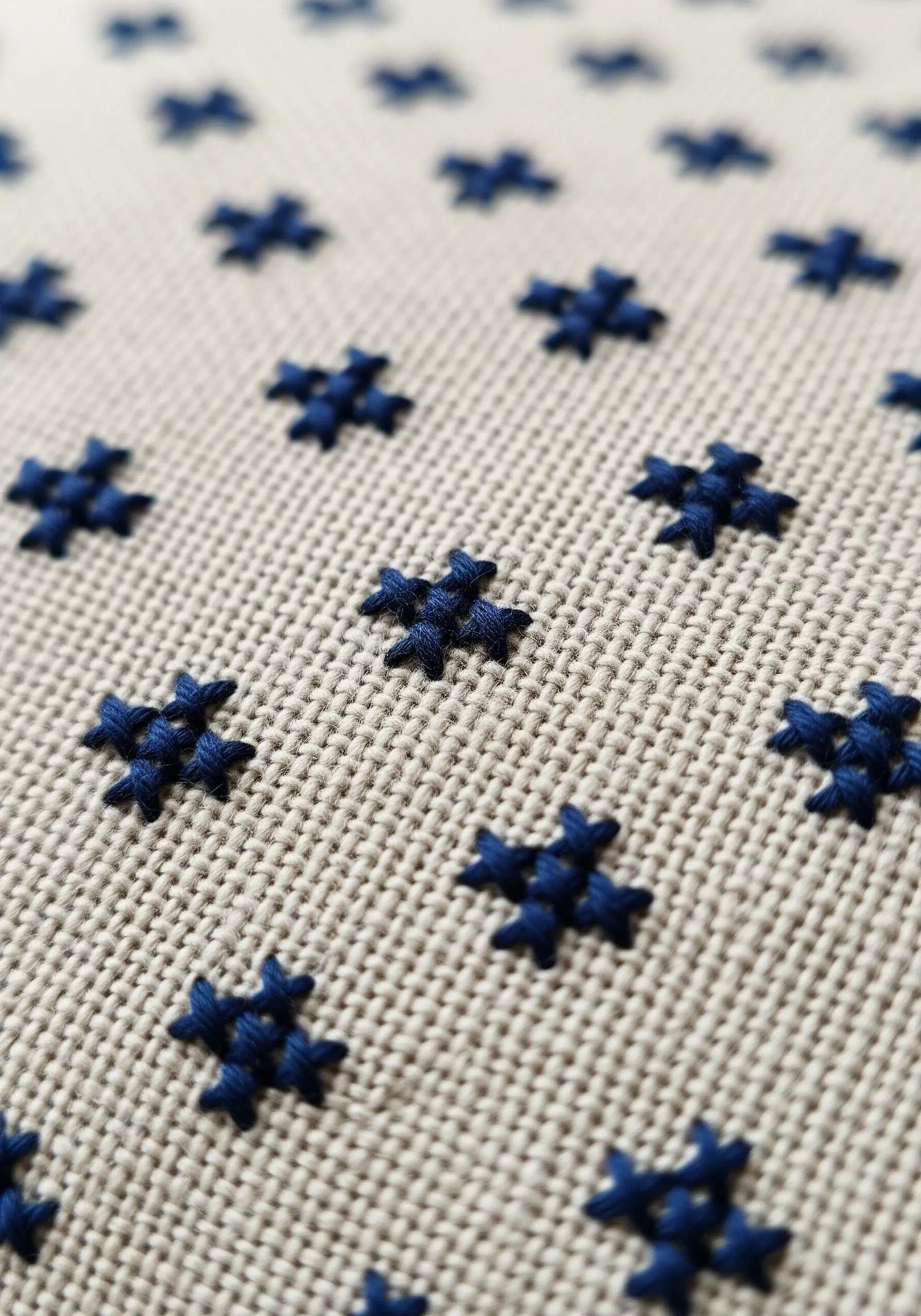 A repeating pattern of small, dark blue star stitches on a neutral fabric.