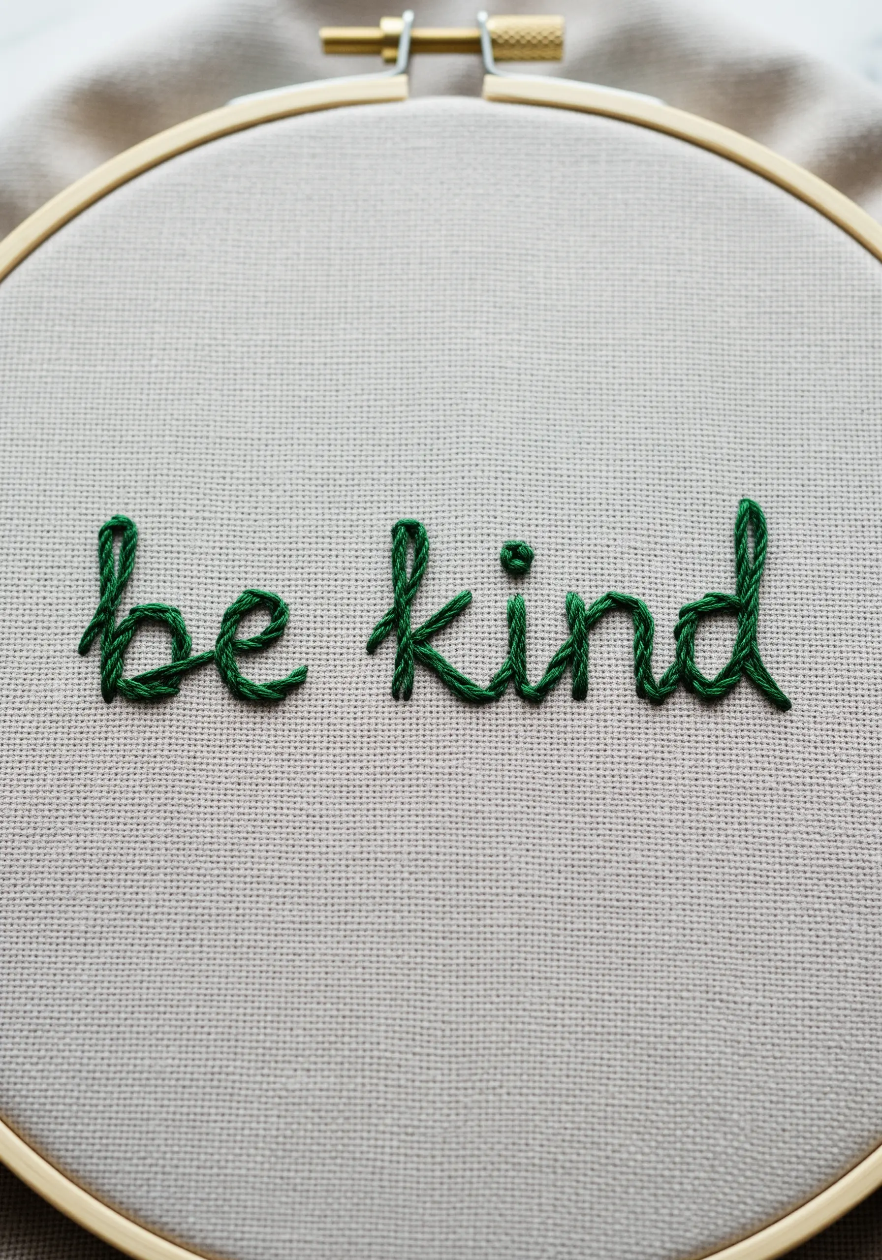 The phrase 'be kind' embroidered in a simple green handwritten style.
