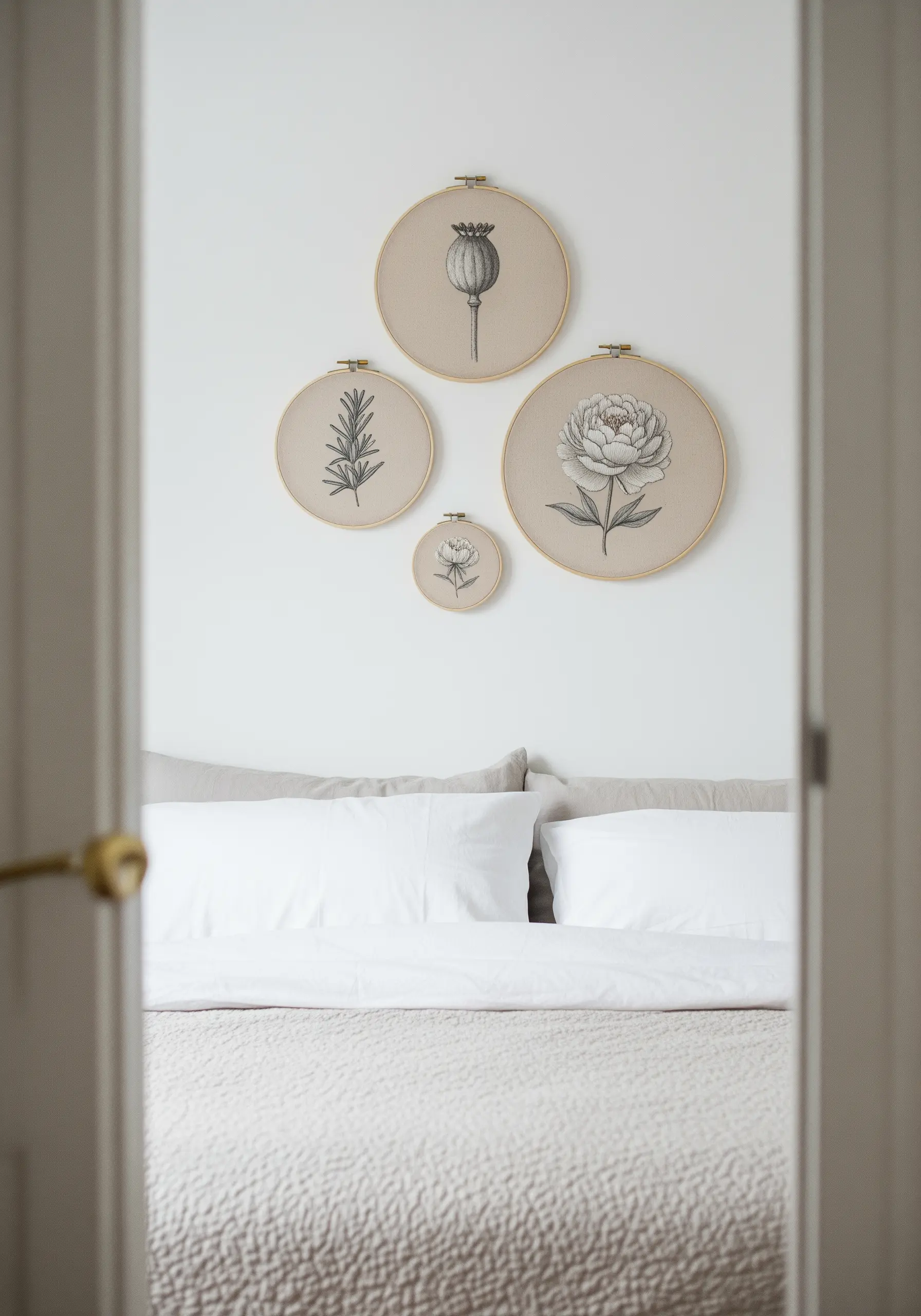 A gallery wall of four embroidery hoops with blackwork botanical illustrations of a poppy, peony, and herbs.