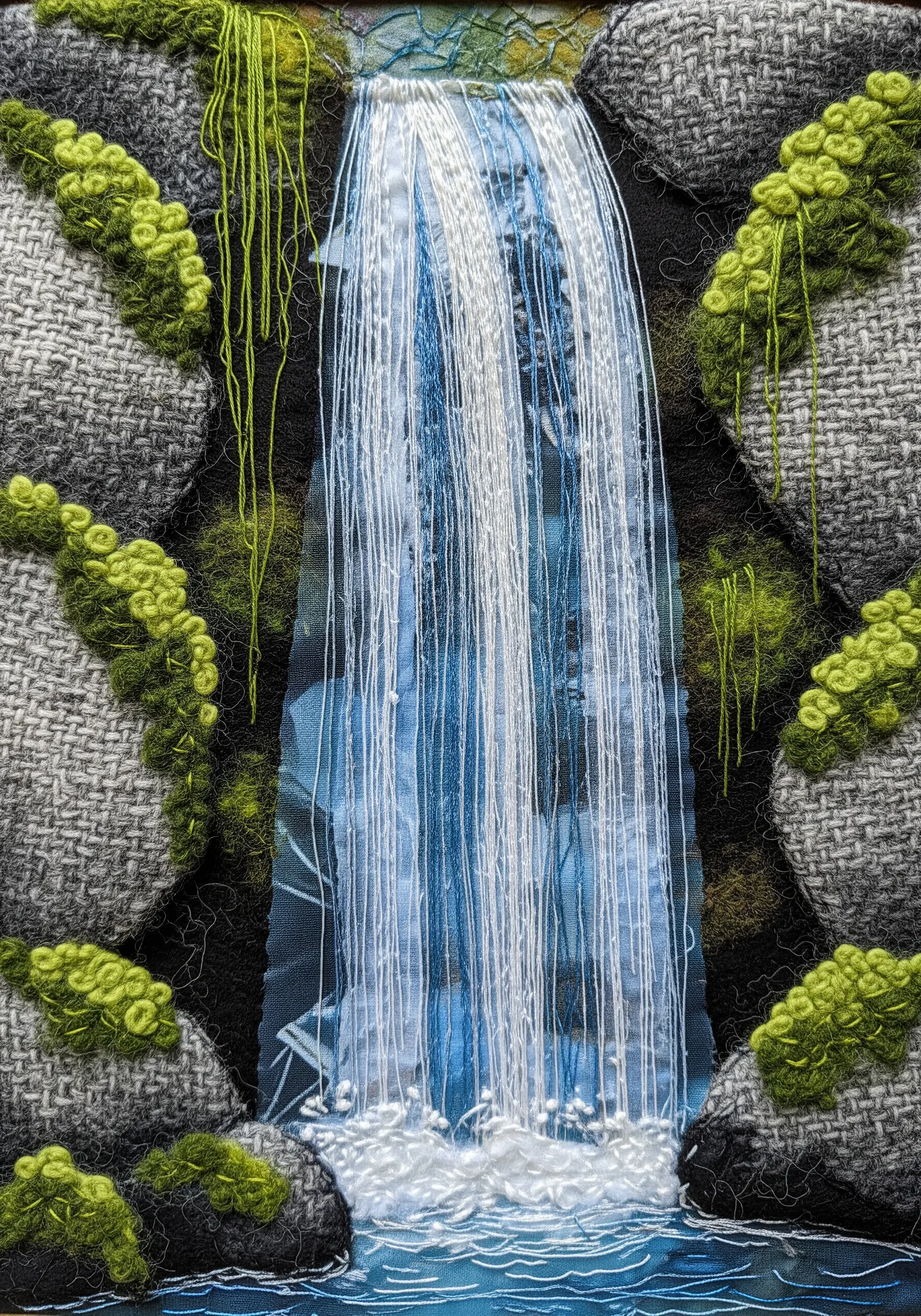 A fabric collage waterfall using loose vertical threads for flowing water.