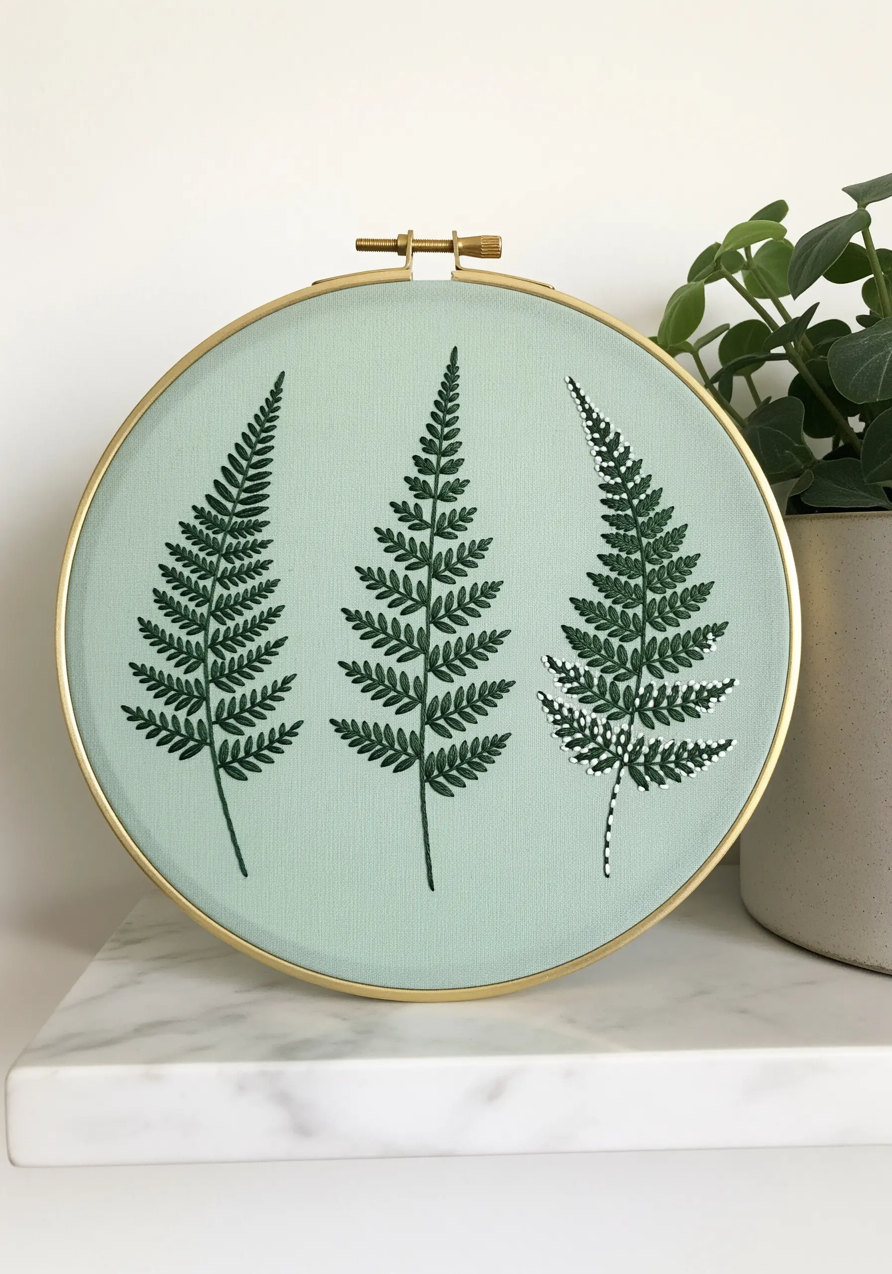 Three embroidered ferns on sage green fabric, showcasing precise fishbone stitches.