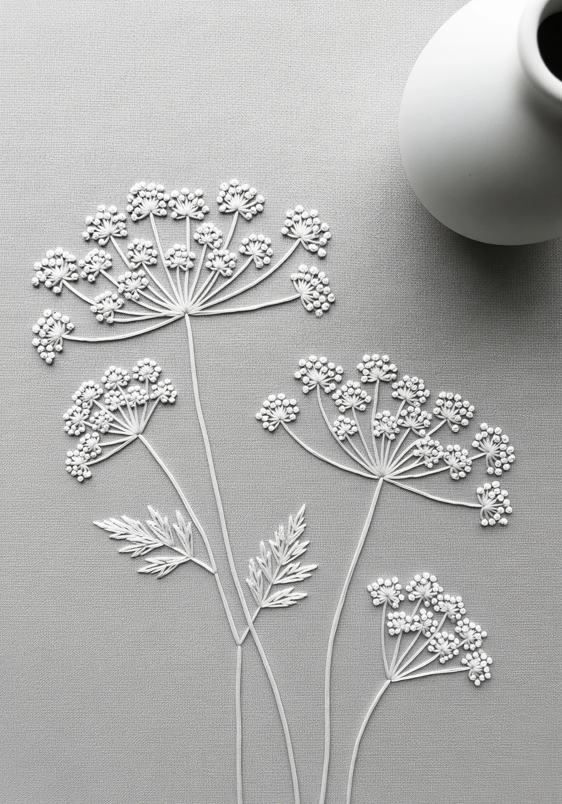 Delicate Queen Anne's lace embroidered entirely in white thread on grey fabric.