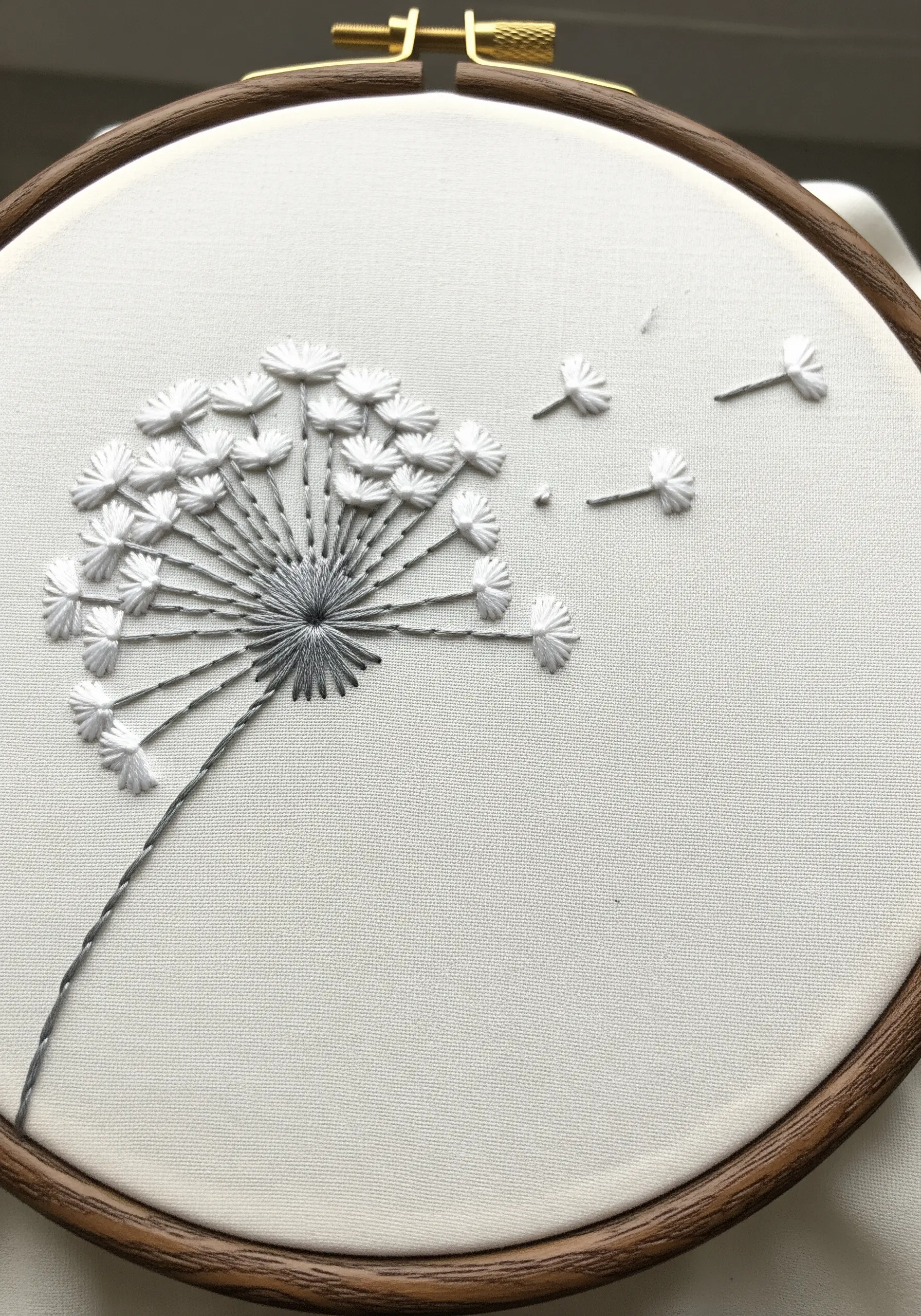 White embroidered dandelion with seeds blowing away in the wind.