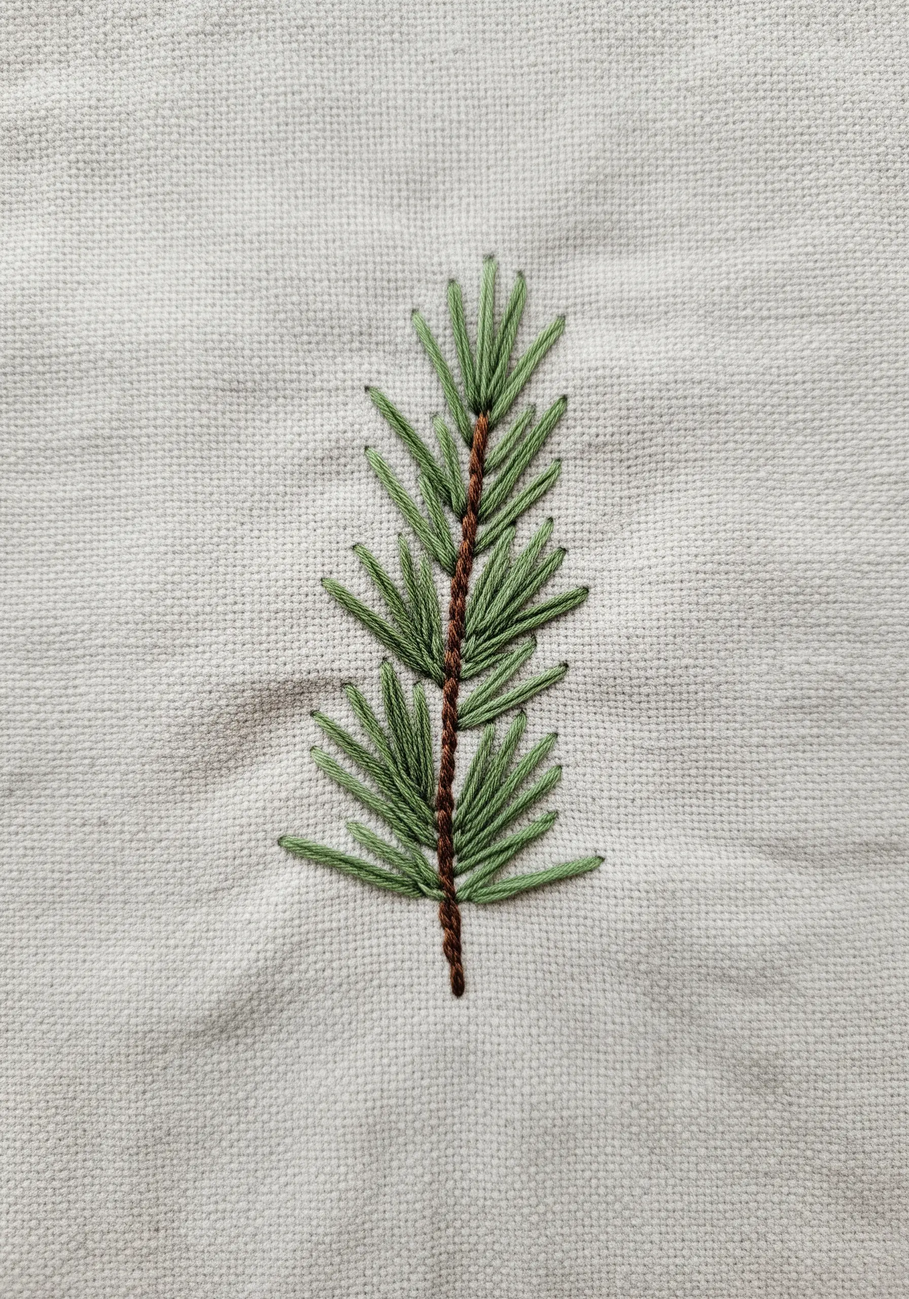 A hand-embroidered pine sprig using fly stitch for needles on a neutral linen towel.