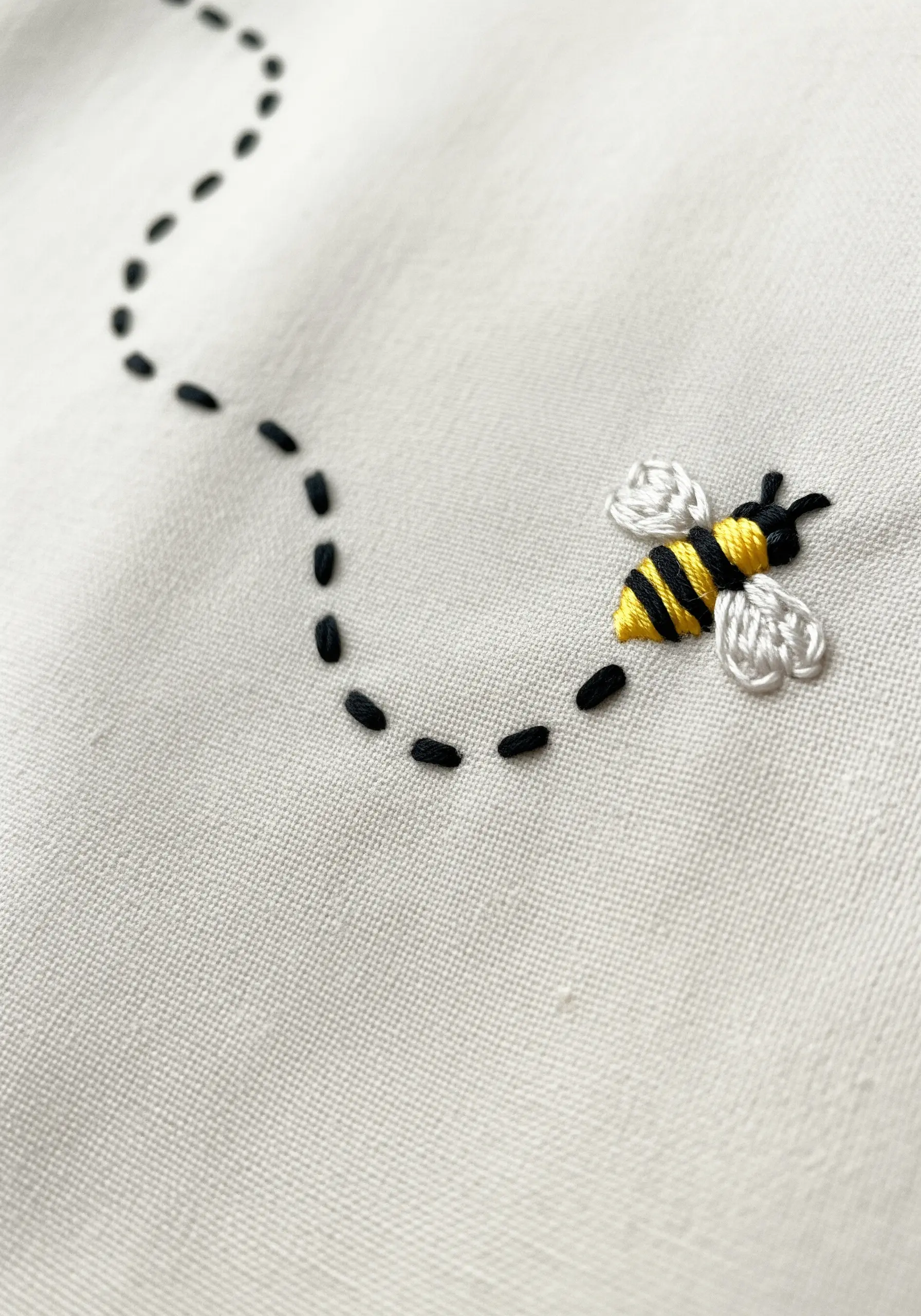 An embroidered bee with a curved, dashed black line indicating its flight path.