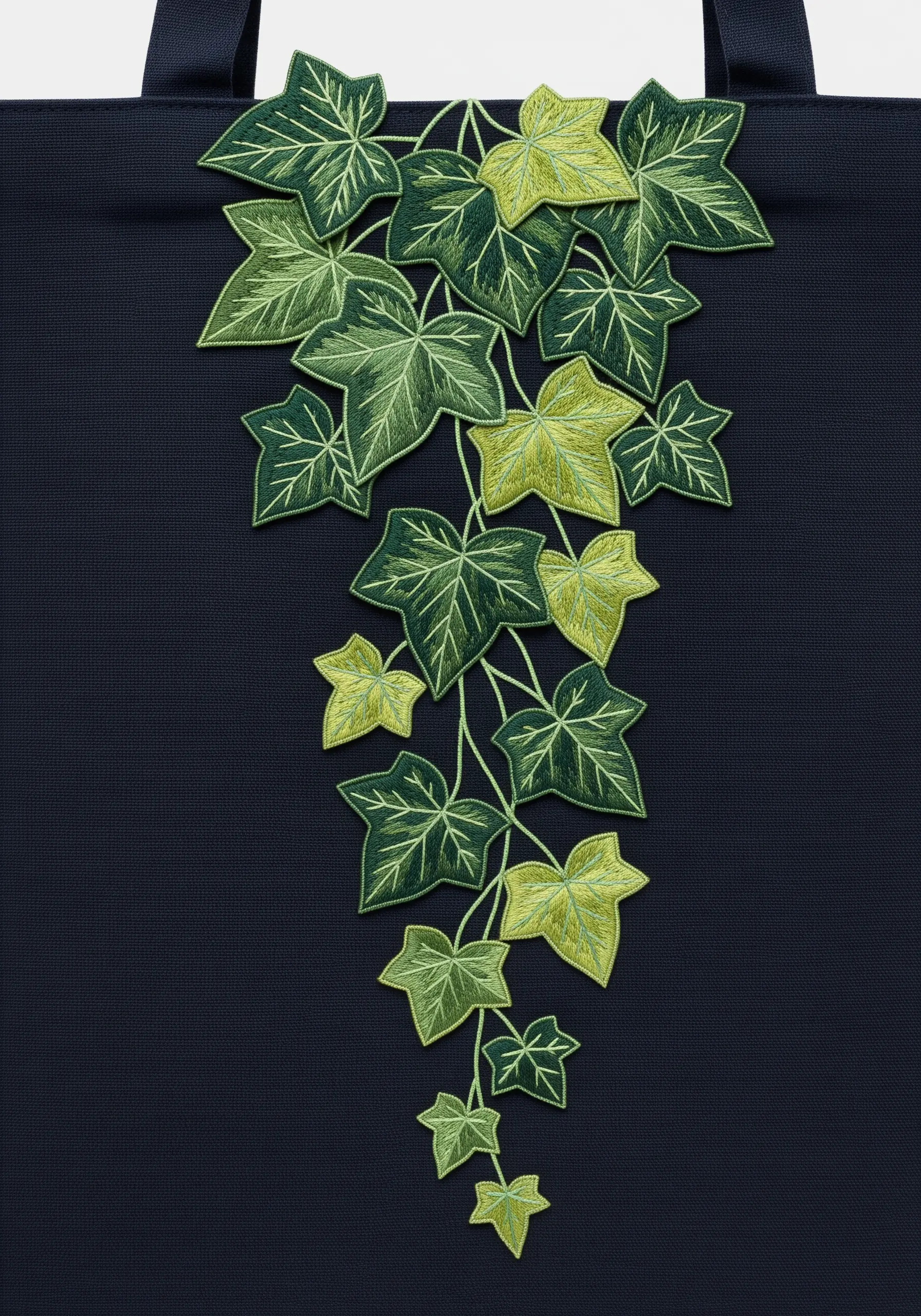 A cascade of embroidered ivy leaves with satin stitch outlines on a navy blue tote bag.