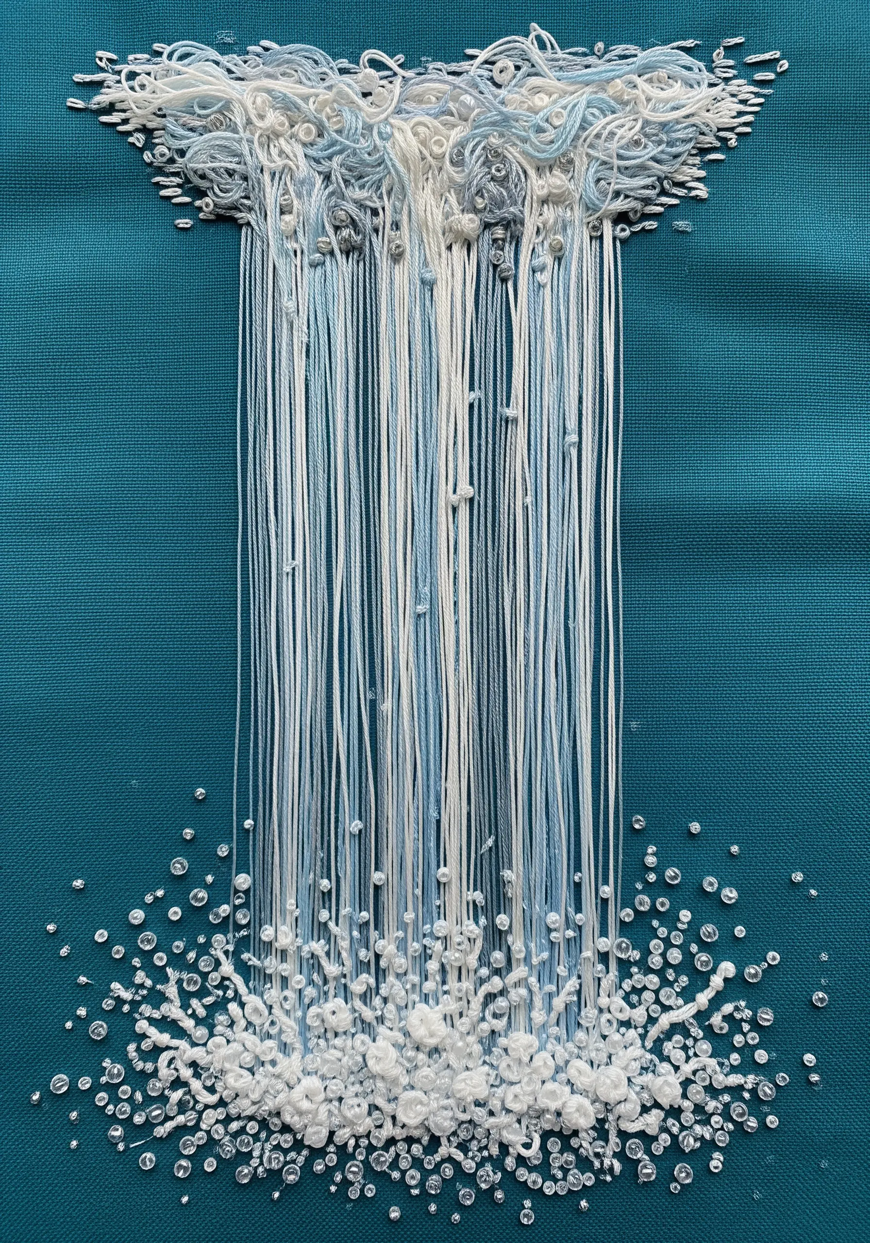Embroidery of a waterfall with loose vertical threads and a base of white knots and beads.