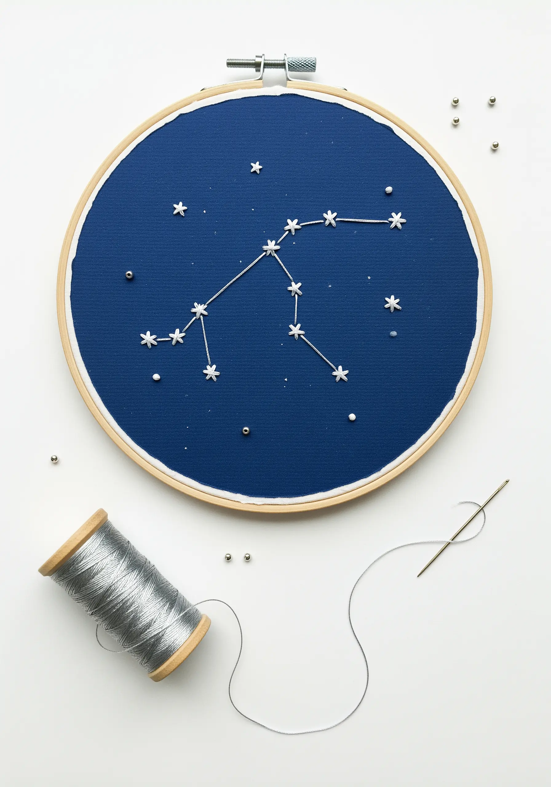 Embroidered constellation on dark blue fabric using silver thread and beads.