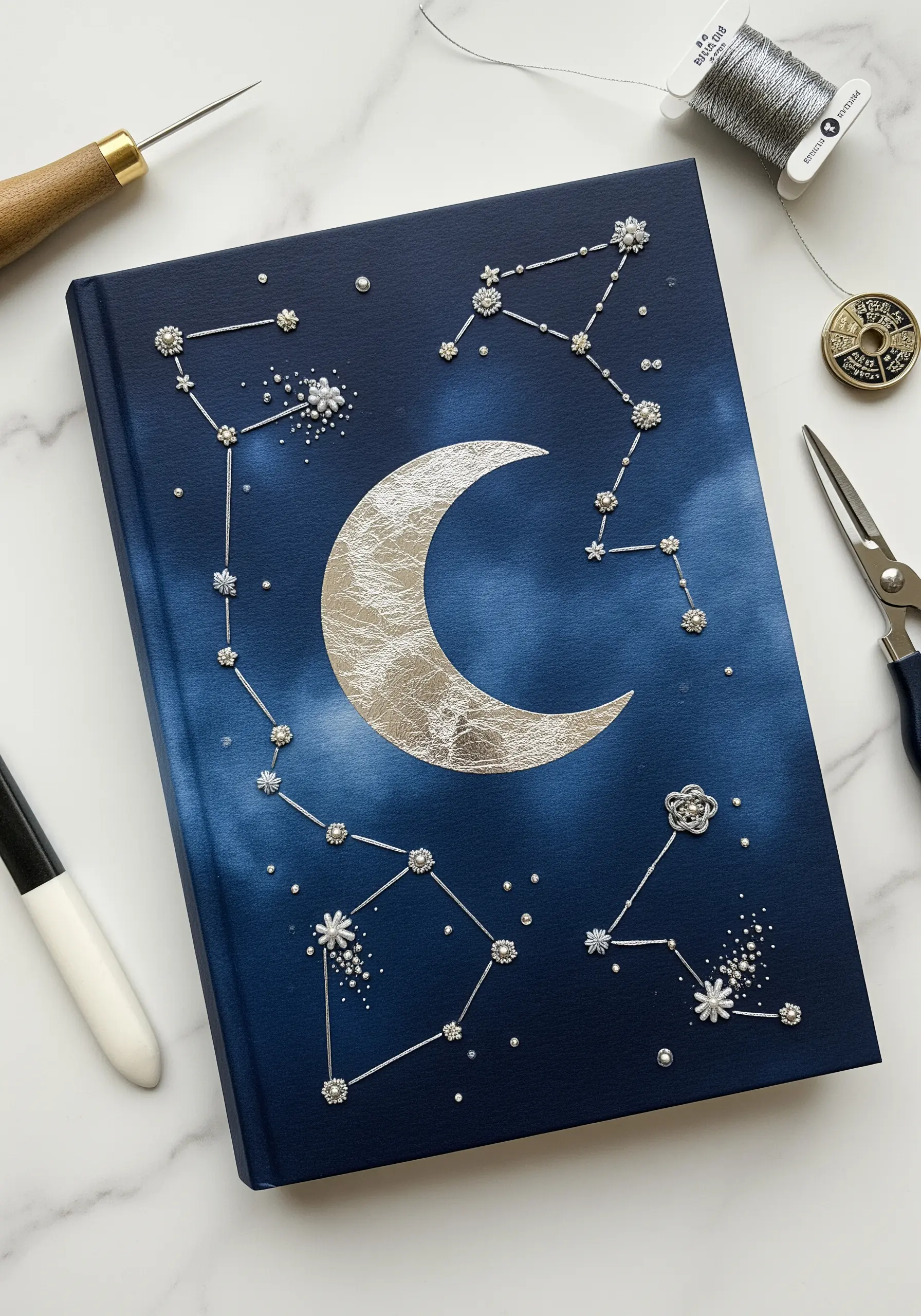 A dark blue journal cover embellished with silver thread constellations and a silver leaf moon.