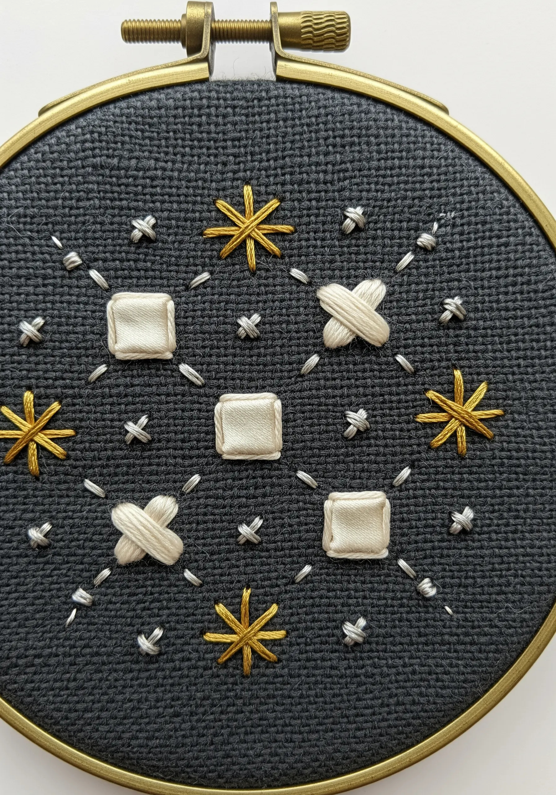 A celestial pattern with padded satin stitch squares and metallic thread starbursts.