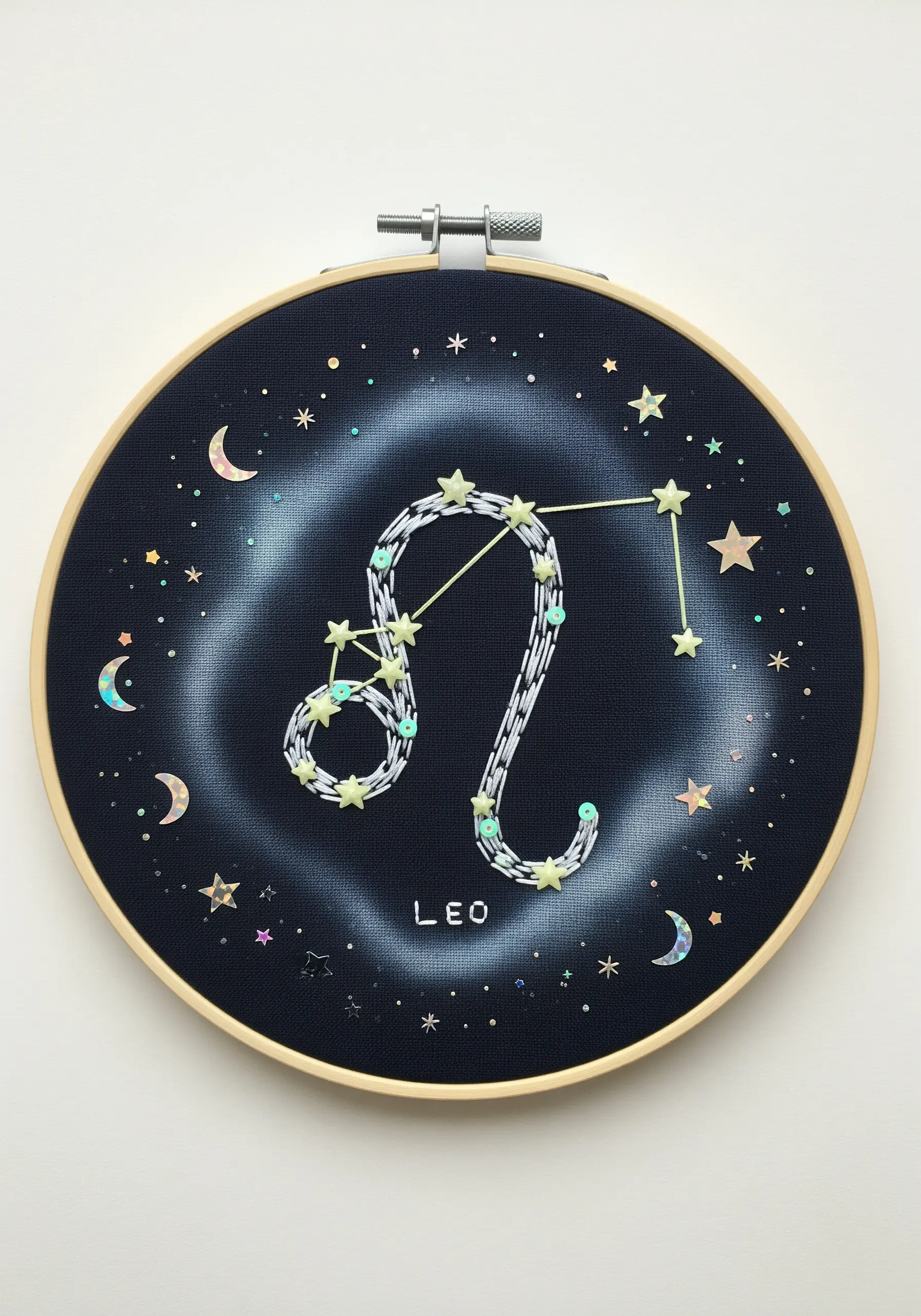 A Leo constellation embroidered on dark fabric with a painted nebula and iridescent sequins for stars.