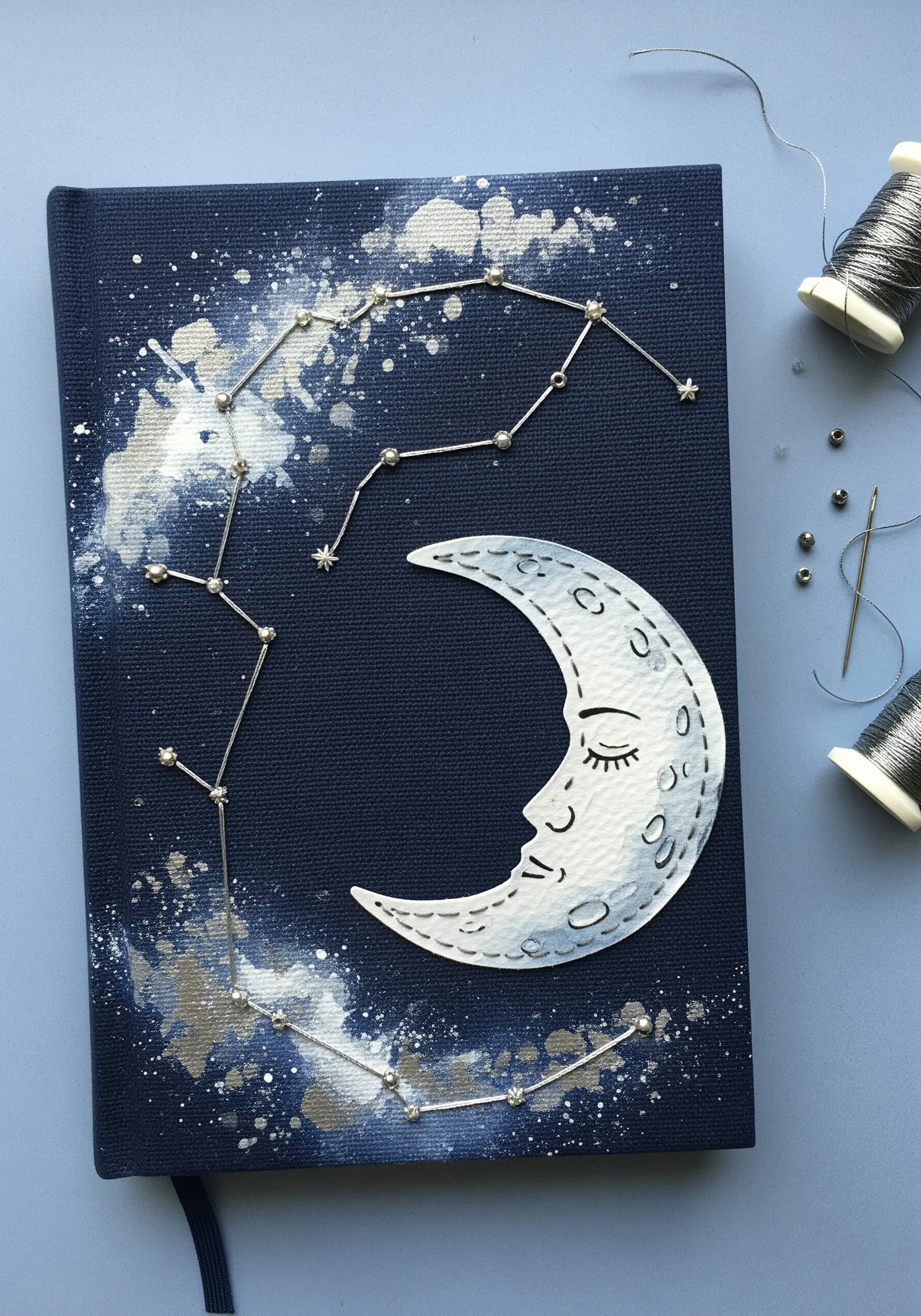 Dark blue journal cover with a silver constellation stitched with beads and a watercolor moon appliqué.