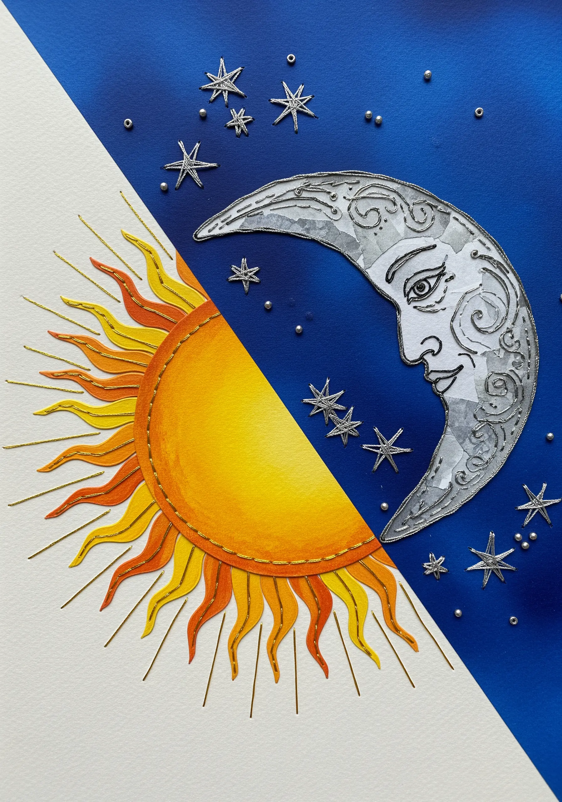 A painted sun and moon design on paper, with outlines and details added in metallic thread.