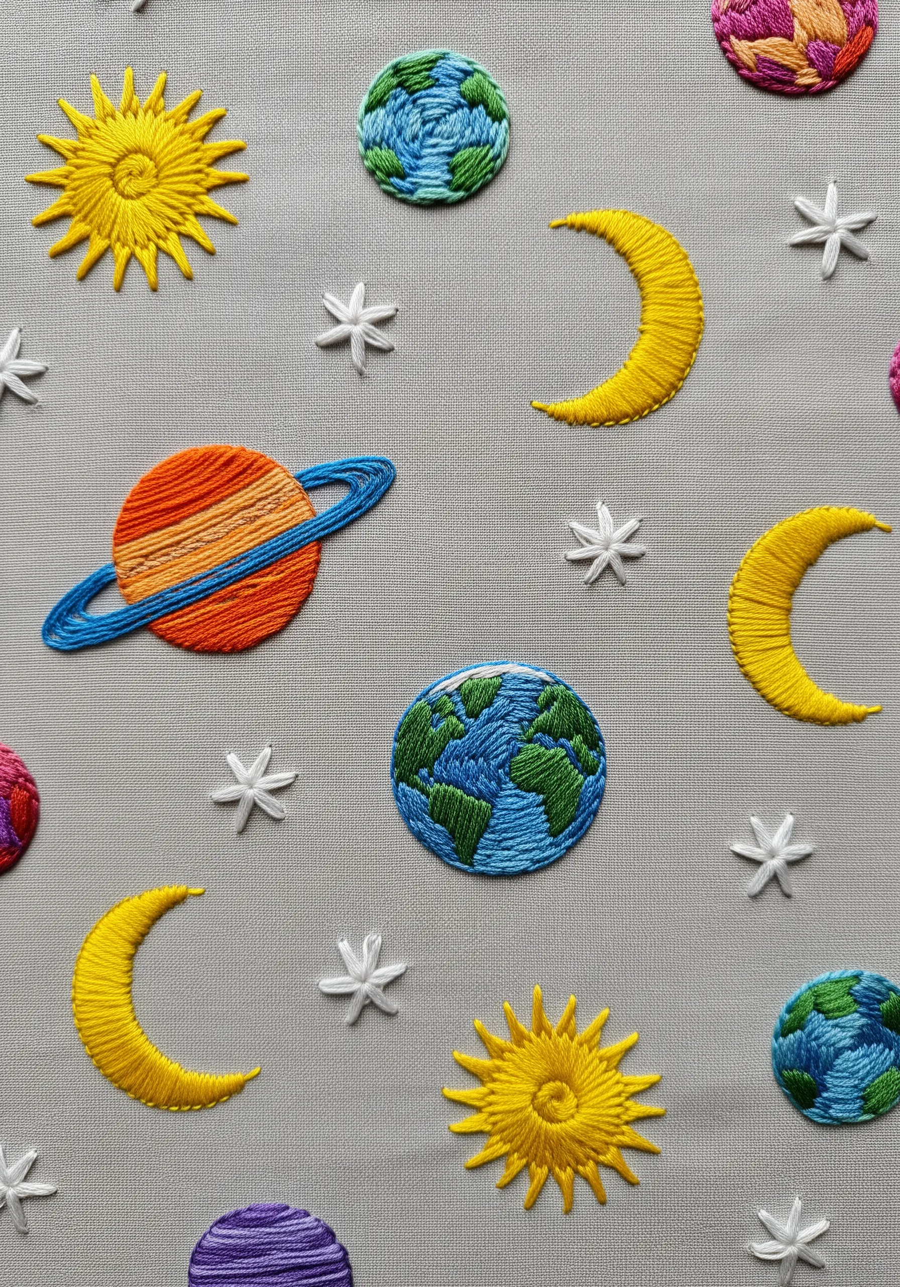 Satin-stitched planets, moons, and suns scattered across grey fabric.