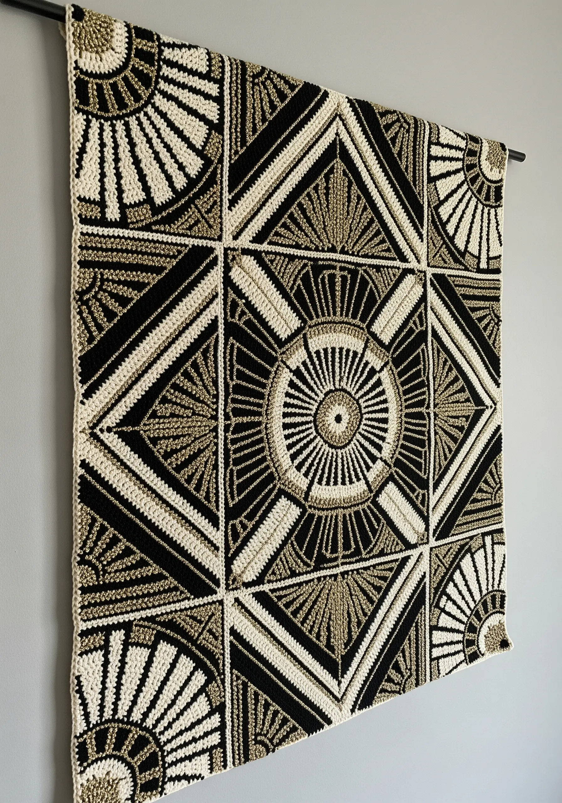 A crocheted wall hanging with a black, cream, and gold Art Deco geometric pattern.