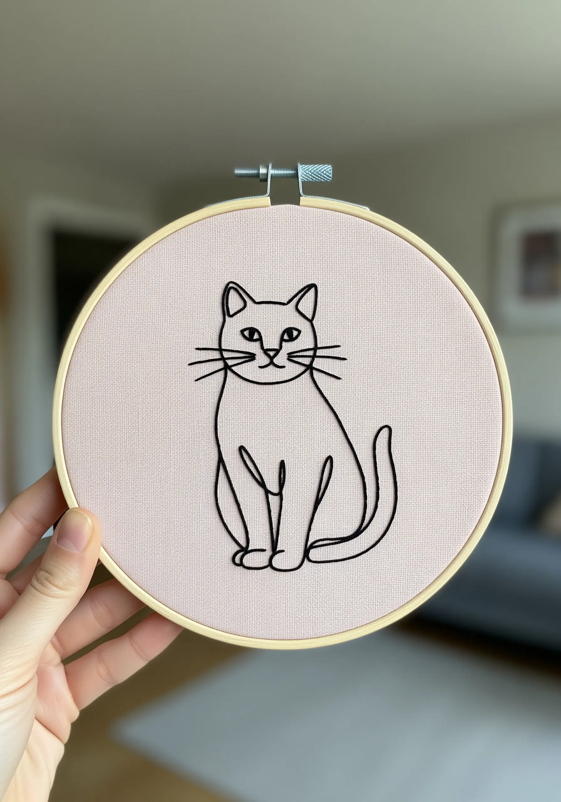 Black line art embroidery of a cat on pink fabric