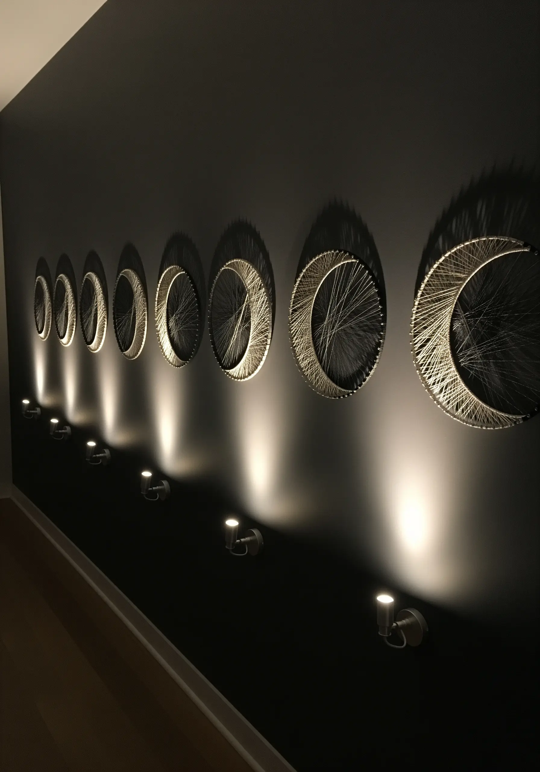 A series of string art hoops depicting the phases of the moon on a dark wall.