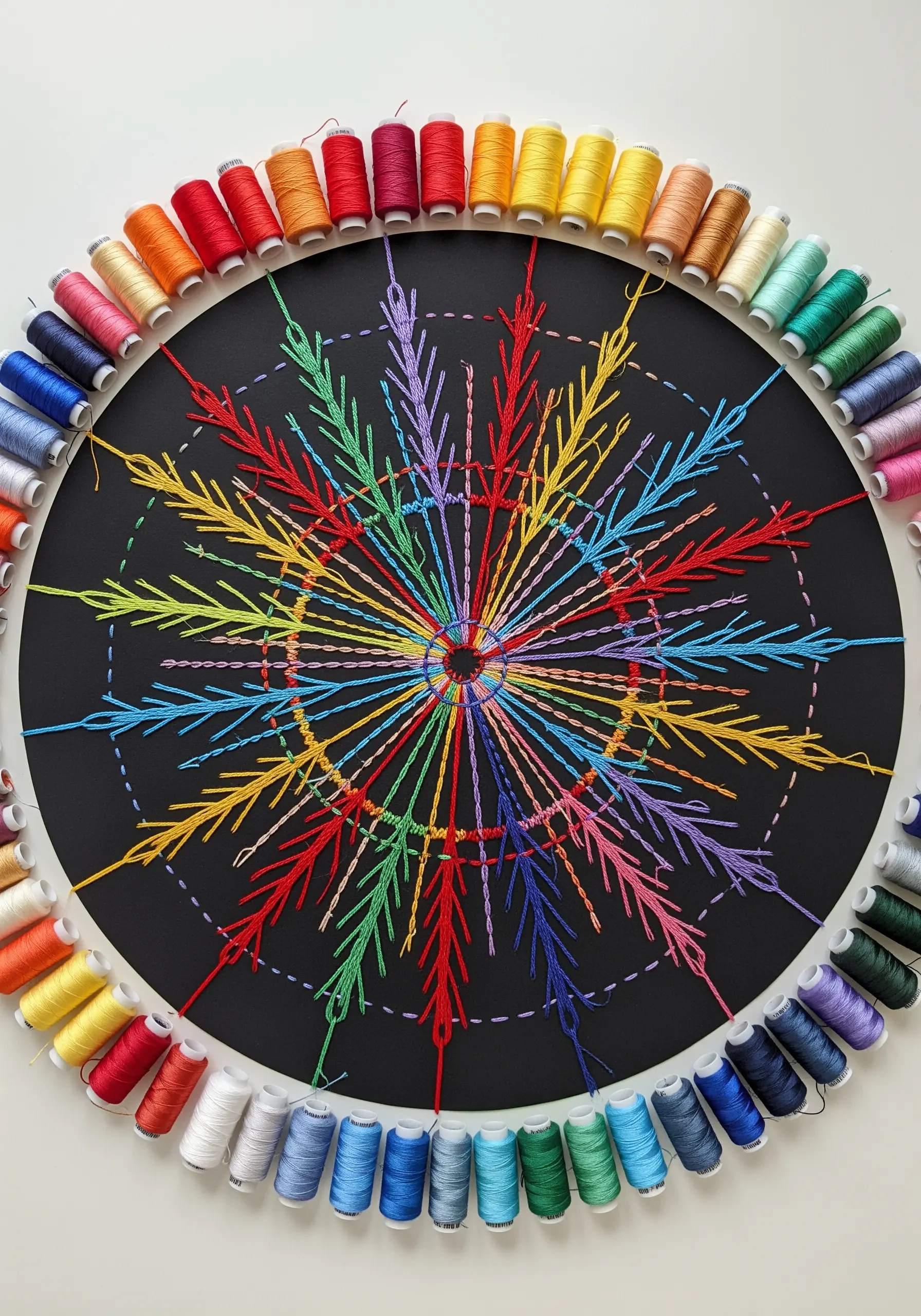 A large, colorful mandala stitched with rainbow threads on a black circular base.