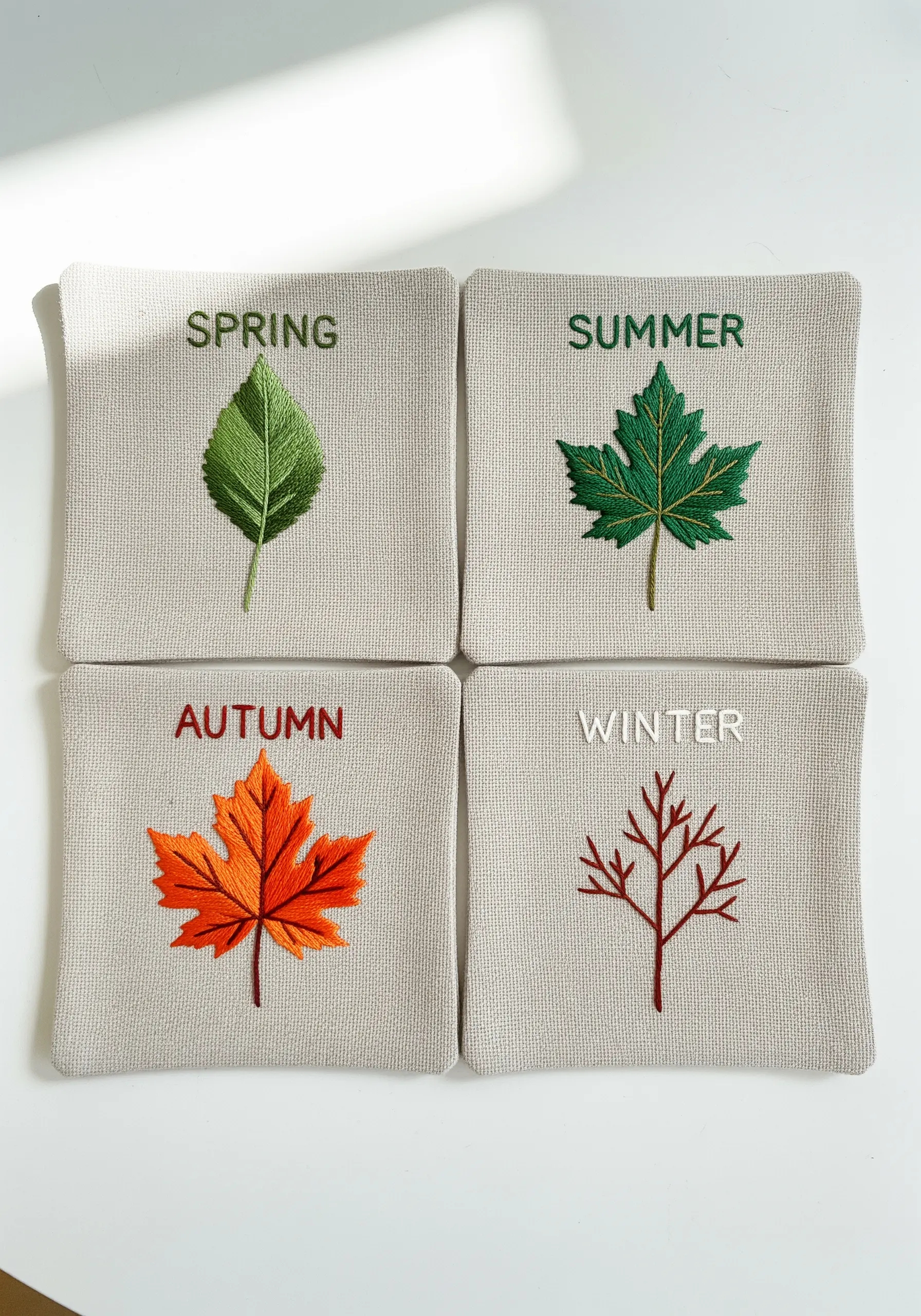 Four embroidered squares, each showing a leaf representing a different season: spring, summer, autumn, winter.